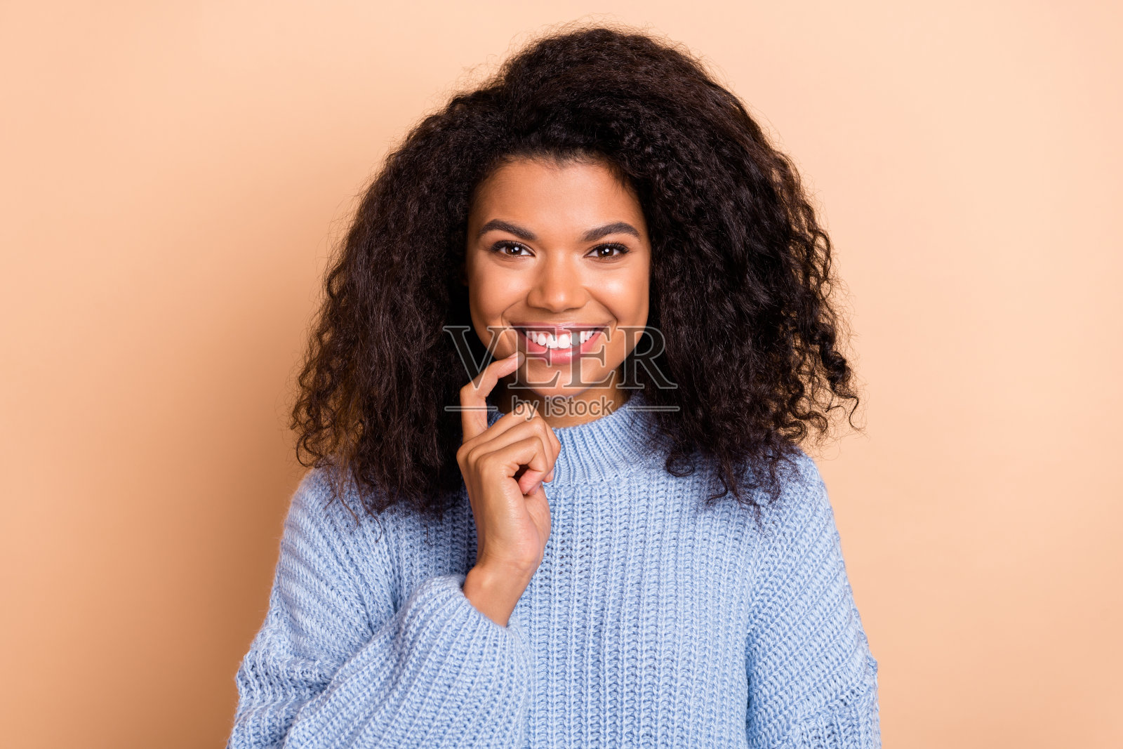 年轻快乐的漂亮女孩用手指触碰下巴，思考中，背景为米色。照片摄影图片