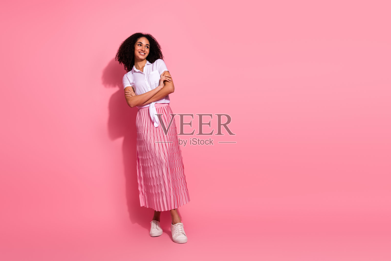 微笑的年轻女性穿着休闲服装，搭配粉色裙子和白色衬衫，站在明亮的粉色背景前。照片摄影图片