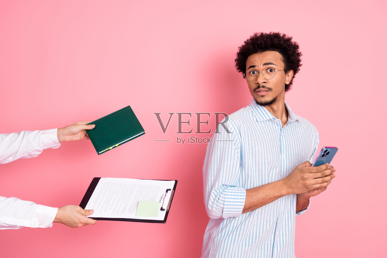 年轻男子穿着休闲服，手持手机，面露惊讶表情，拒绝文件，背景为粉色。照片摄影图片