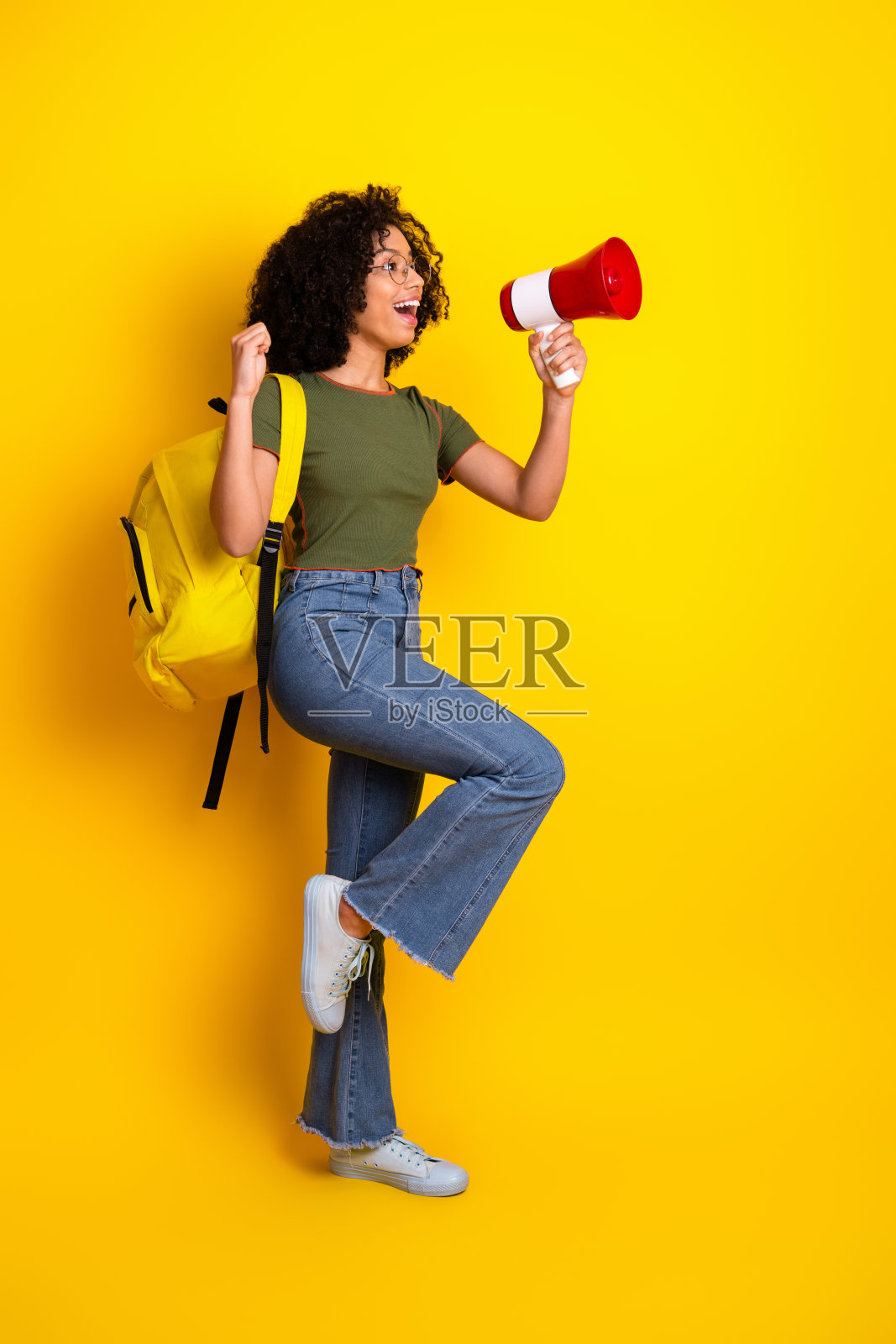 快乐的年轻女性在黄色背景下手持扩音器，表达兴奋并传播快乐照片摄影图片