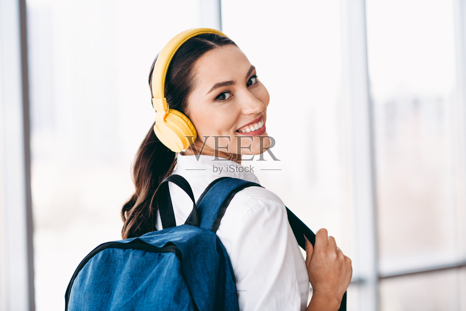 迷人的女性背着背包，戴着耳机，在明亮的现代城市环境中自信地微笑照片摄影图片