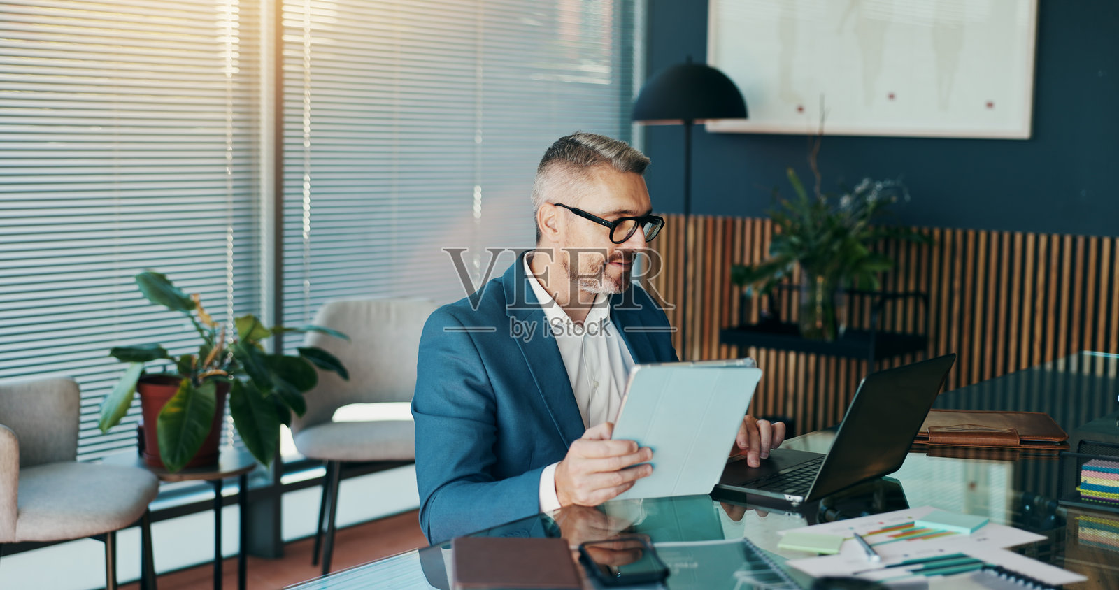 办公室里的商人使用平板电脑、笔记本电脑和书籍，适合股票经纪人、客户经理或预算报告。市场监控、交易风险和利润增长，适合成熟人士进行投资规划。照片摄影图片
