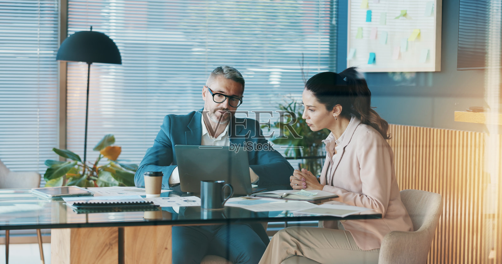 办公室内的文件、笔记本电脑和商务人士正在讨论公司投资交易。计算机、文件和财务经理与投资客户在工作场所进行会议，讨论分红报告。照片摄影图片