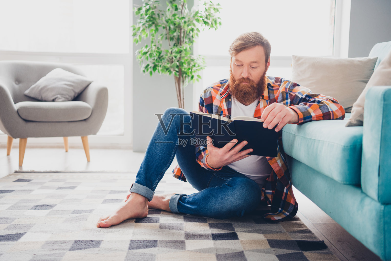 留着胡子的男人在阳光透过窗户洒入的舒适客厅地板上阅读一本书照片摄影图片