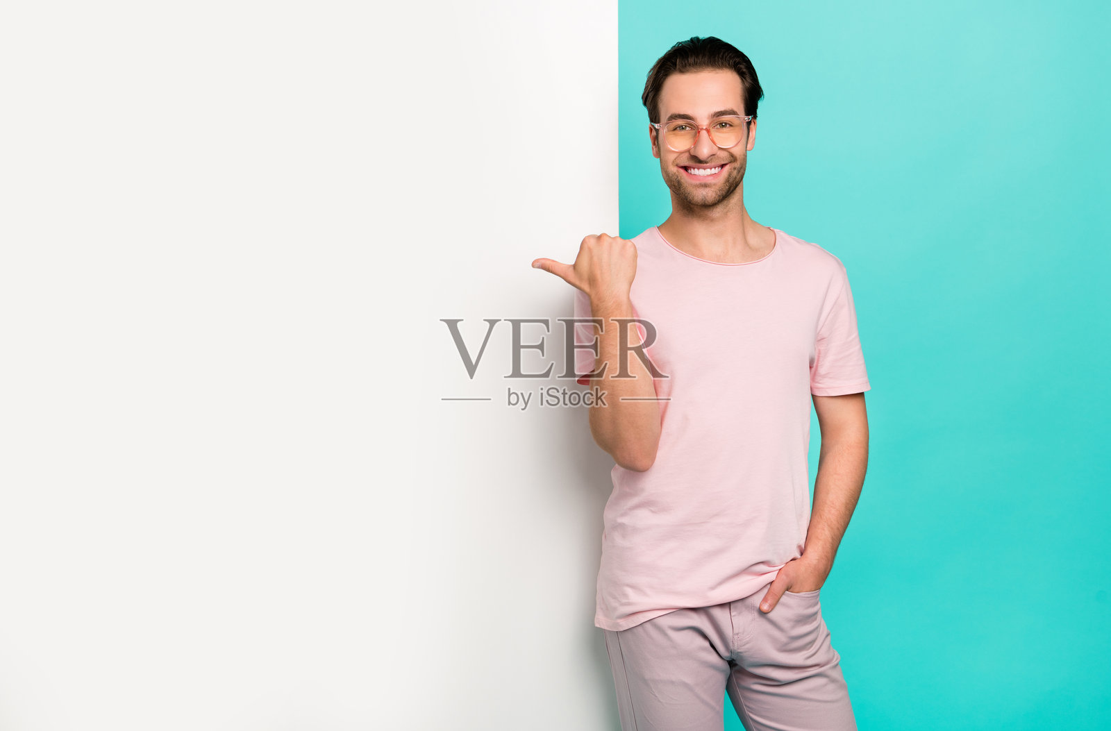 年轻男子推广员用拇指指向空白区域，适合广告宣传，背景为青绿色。照片摄影图片