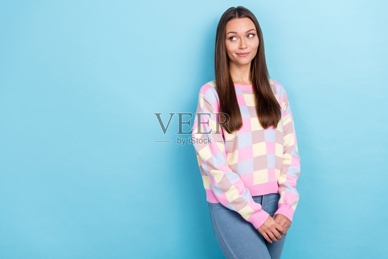 可爱的积极梦幻女孩穿着休闲毛衣和牛仔裤，望向空旷的空间，背景为蓝色。照片摄影图片