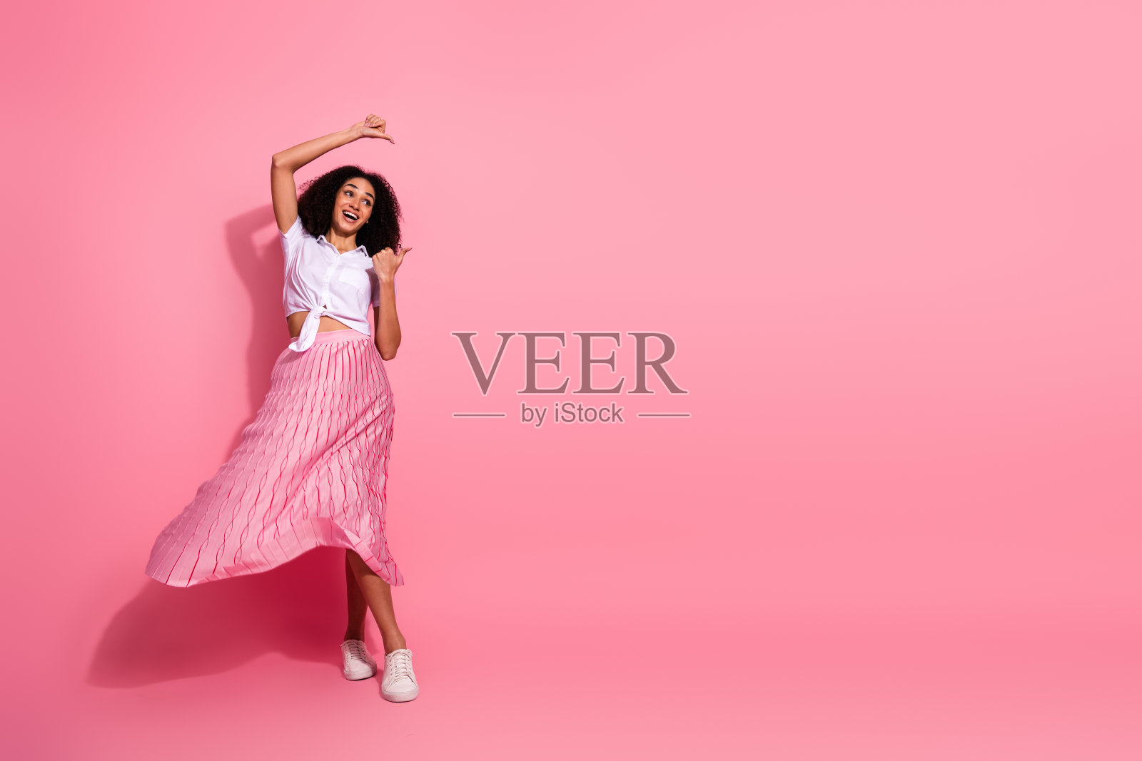 快乐的年轻女性穿着时尚休闲服装，在充满活力的粉色背景前欢快地舞动。照片摄影图片