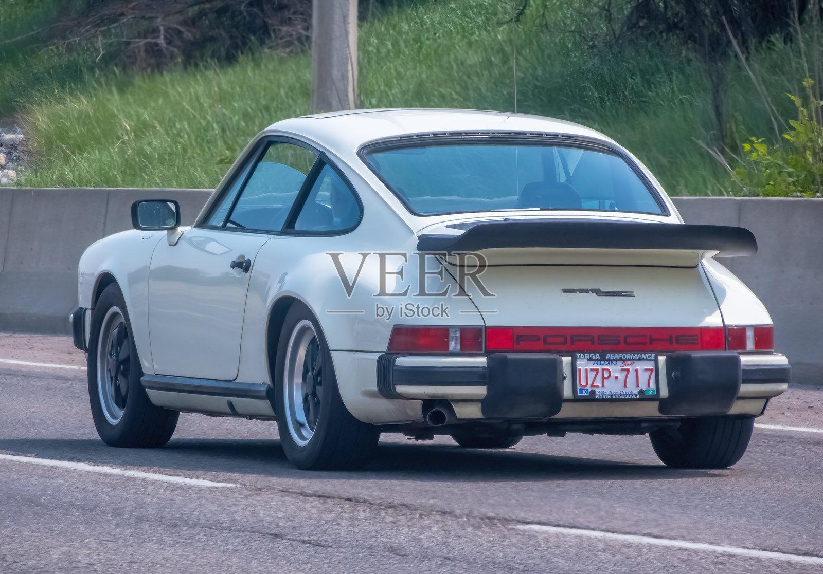 一辆经典的白色保时捷911，展示其永恒的设计和标志性的后扰流板，驰骋在道路上，象征着汽车遗产和性能。照片摄影图片