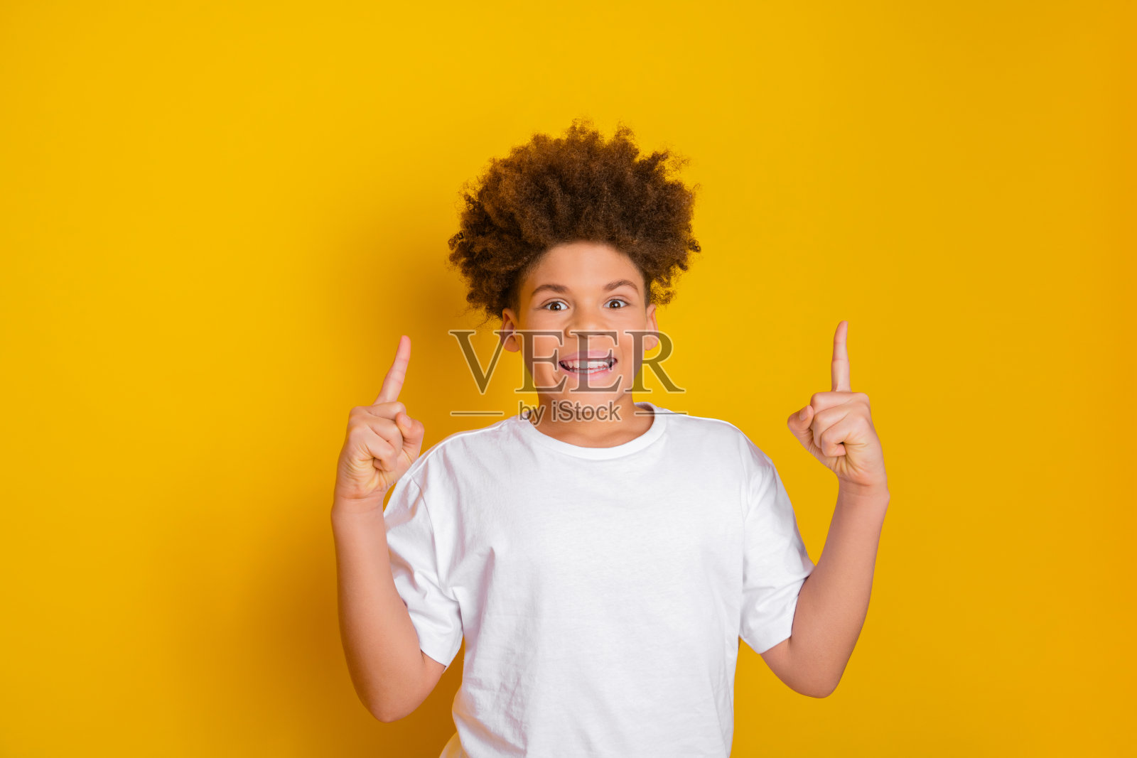 微笑的年轻男孩在充满活力的黄色背景上做出好奇的手势，表达快乐和活力照片摄影图片