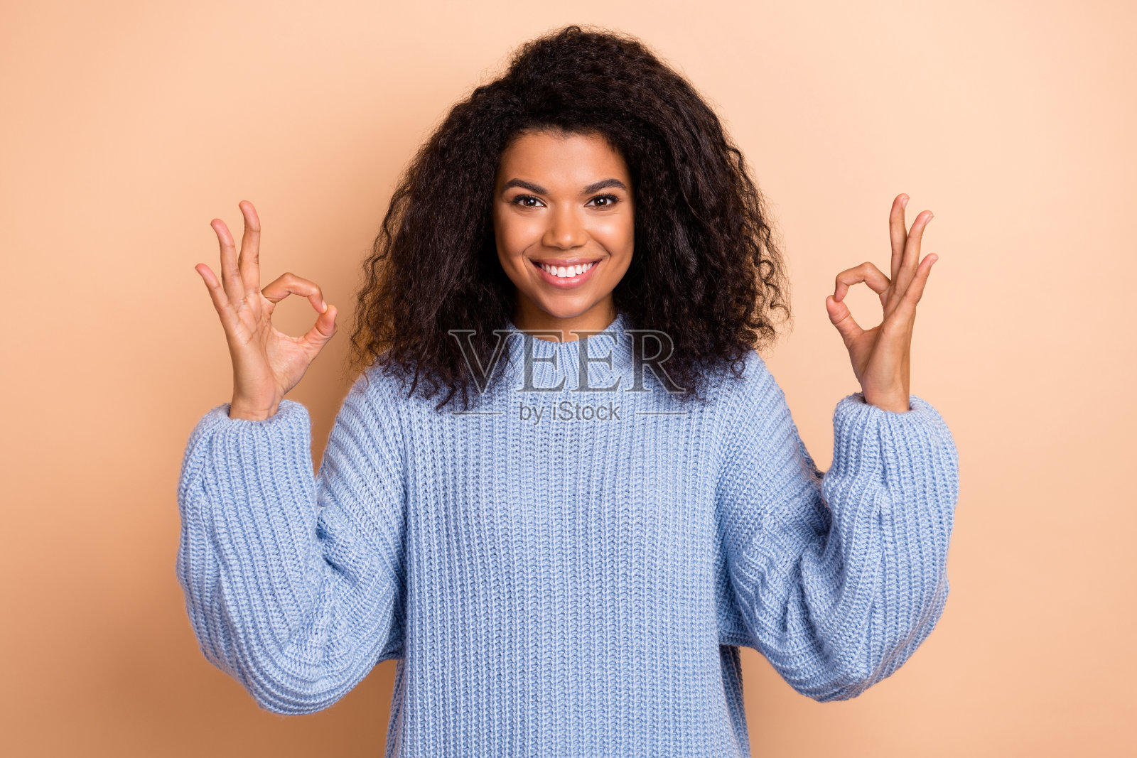 年轻快乐的女孩用手指做出“好”的手势，赞同推广，背景为米色。照片摄影图片