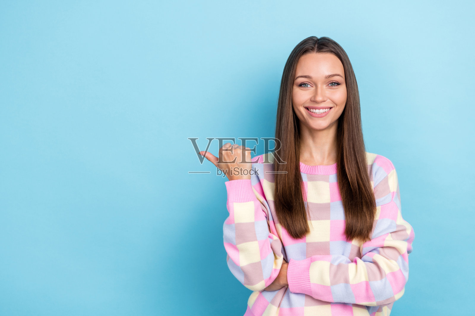 穿着休闲服的快乐推广员女士指着空白处，背景为蓝色。照片摄影图片