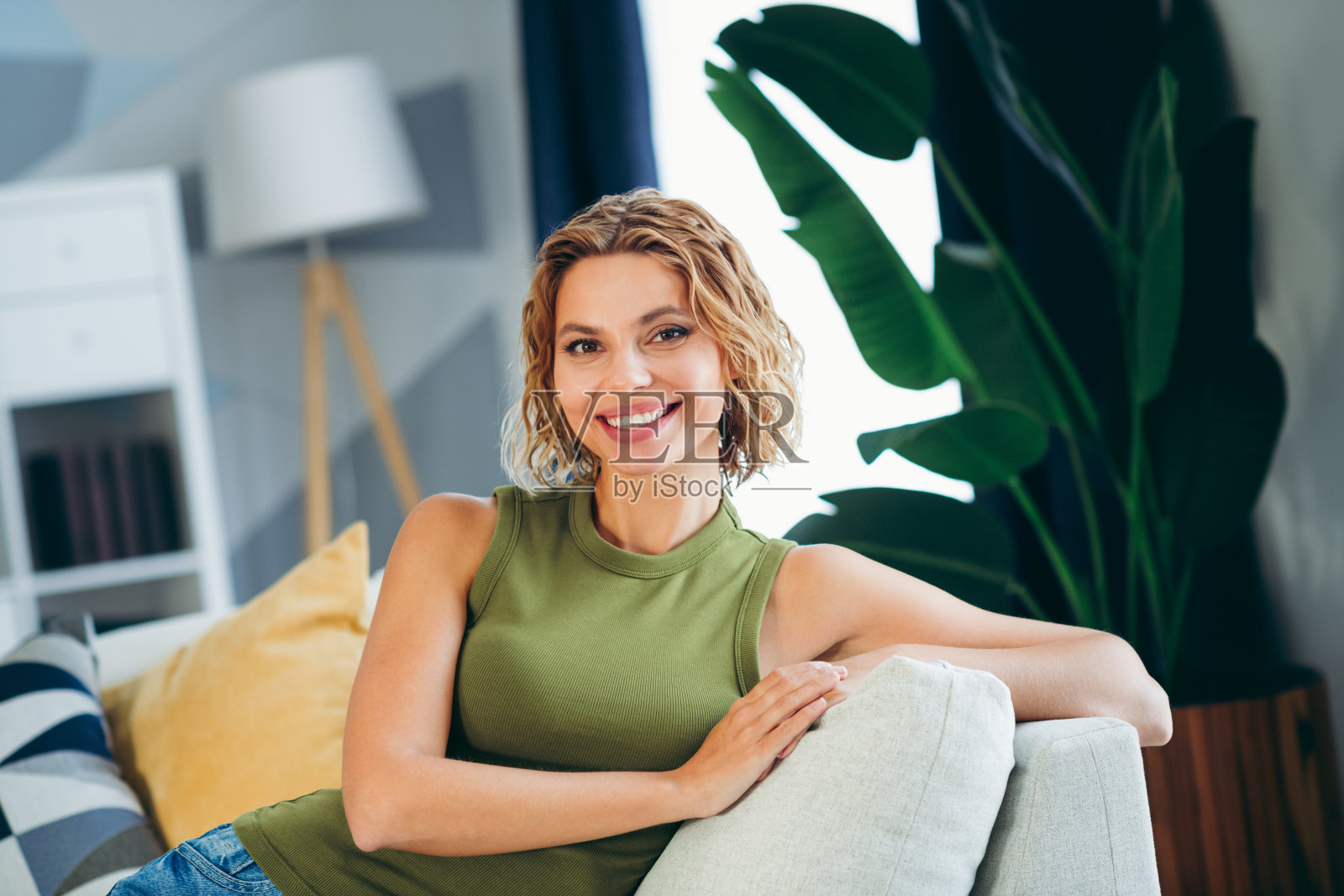 迷人的年轻女性在室内放松，坐在一个温馨的客厅沙发上，周围有生动的装饰和阳光。照片摄影图片