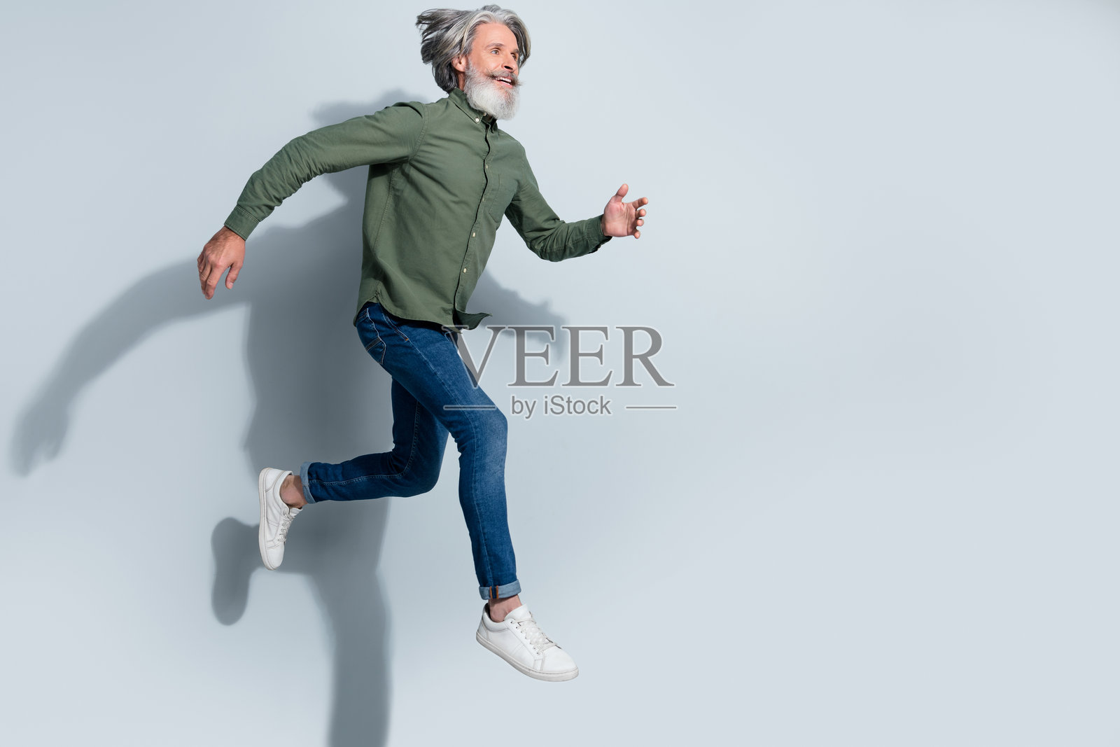 穿着卡其色衬衫的英俊退休男士在灰色背景下高高跳起，奔跑在空旷的空间中。照片摄影图片