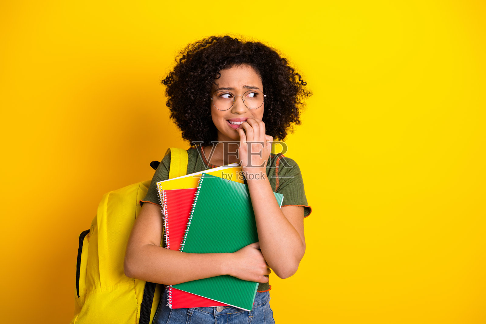 自信的年轻女学生，充满活力的风格，背着五彩斑斓的笔记本和背包，背景为黄色。照片摄影图片