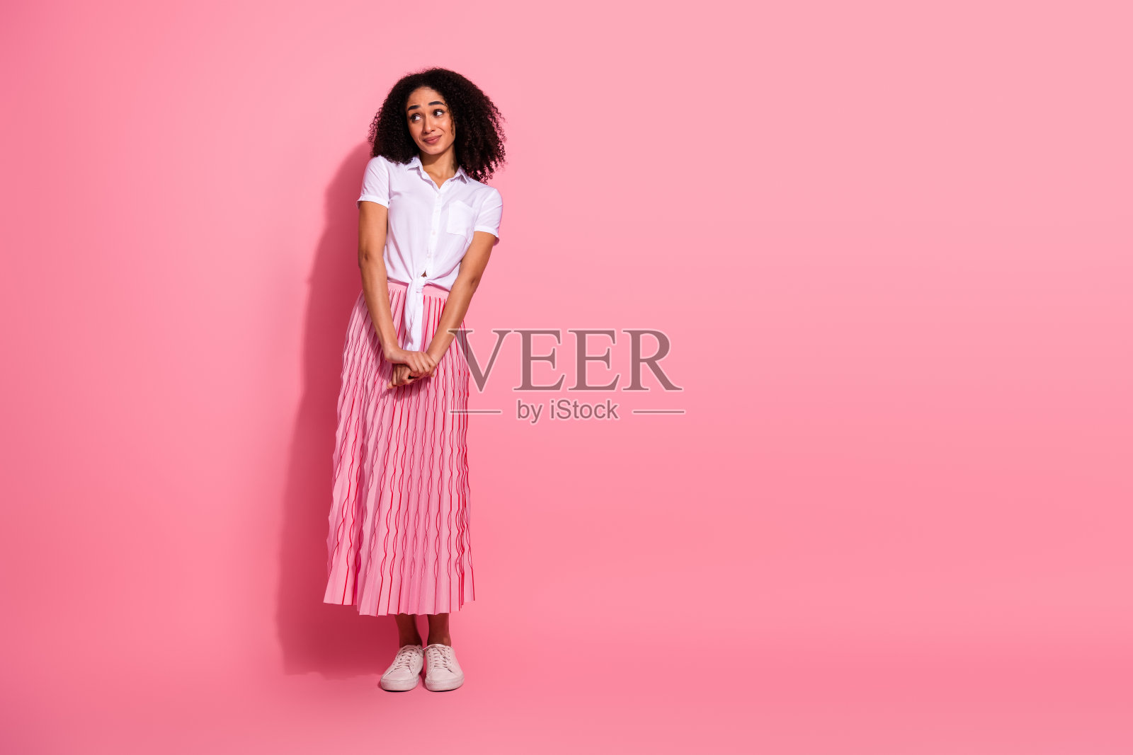 穿着褶皱粉色裙子的时尚女性，背景为纯粉色，展示适合休闲穿着的时尚夏季潮流。照片摄影图片