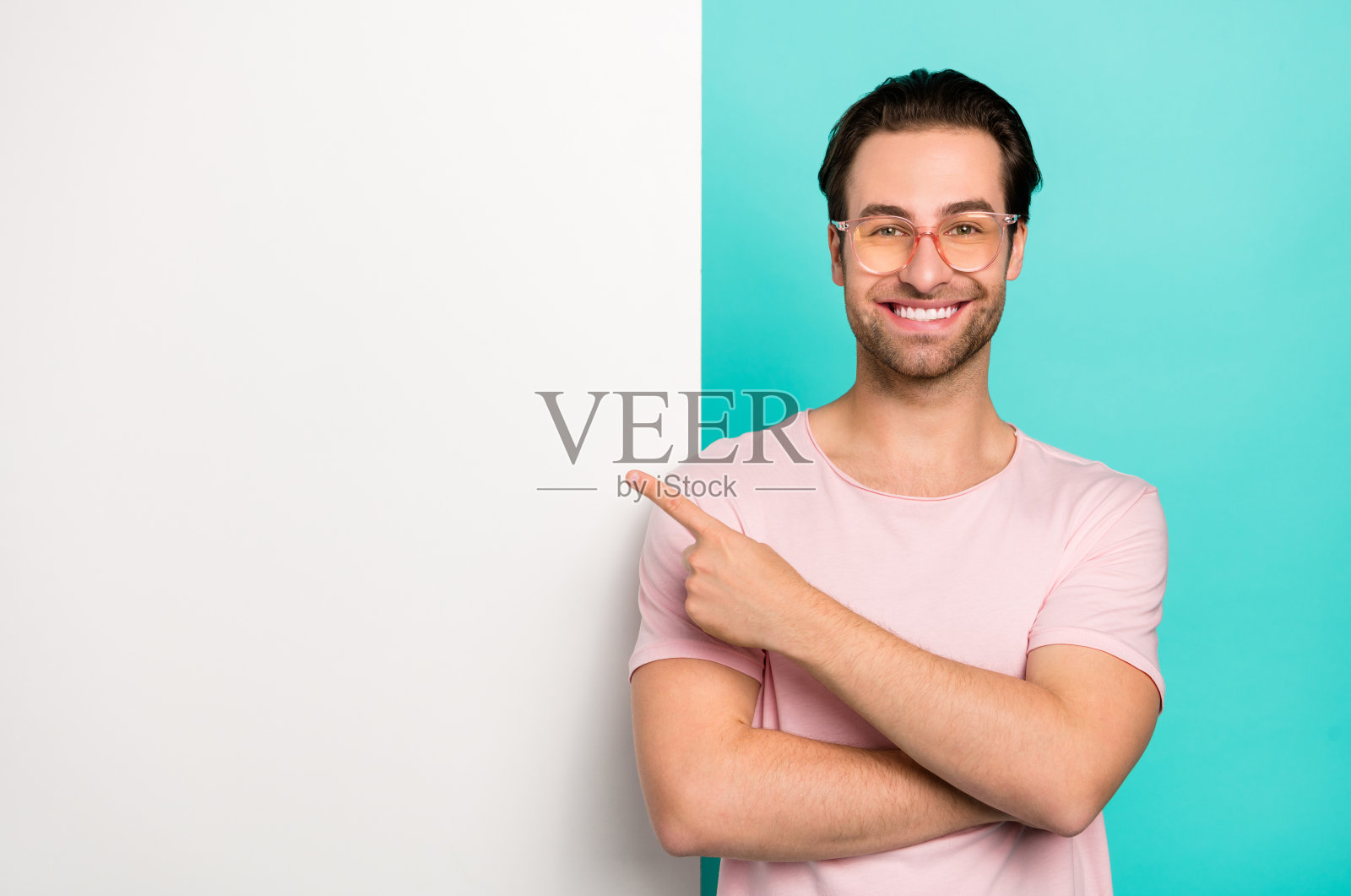 年轻男子用手指指向空白处，推荐选择，背景为青绿色。照片摄影图片