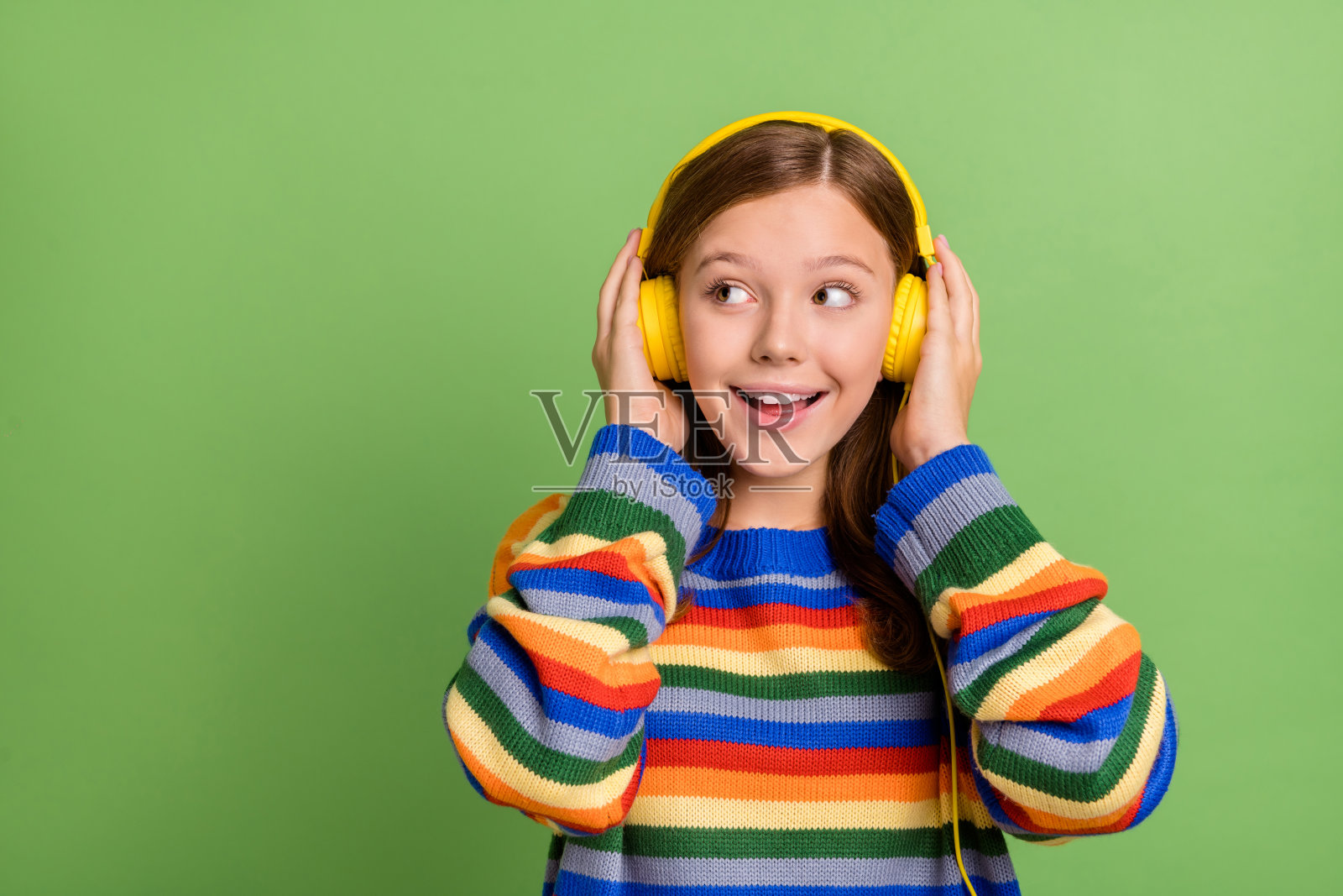 迷人的快乐女孩在明亮的绿色背景下聆听流行音乐单曲，旁边留有空白空间。照片摄影图片