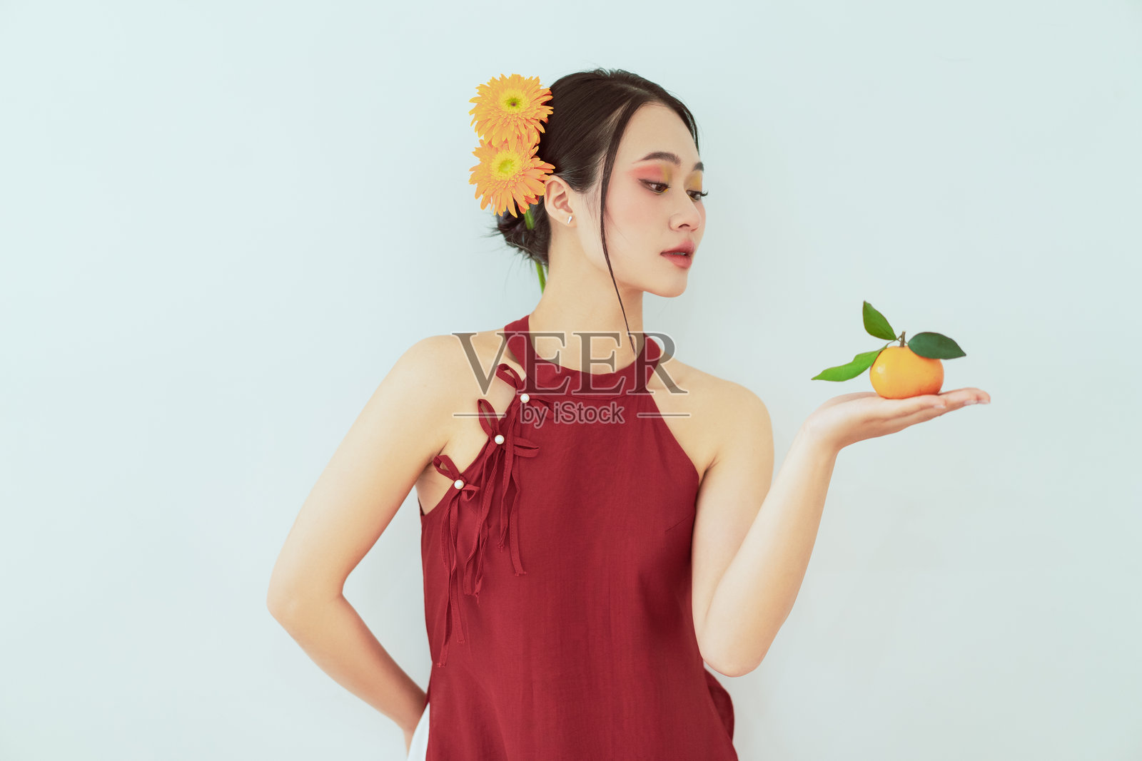 穿着红色连衣裙的女人手持带叶子的橙色水果，背景简约。照片摄影图片