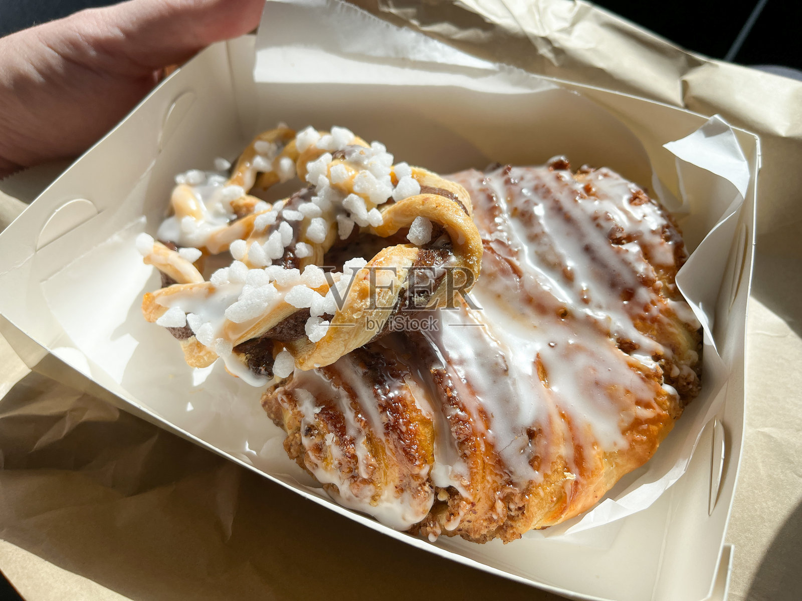 一个白色的糕点盒里装着一块撒有糖霜的榛子丹麦 pastry，顶部有巧克力扭结和岩盐糖。照片摄影图片