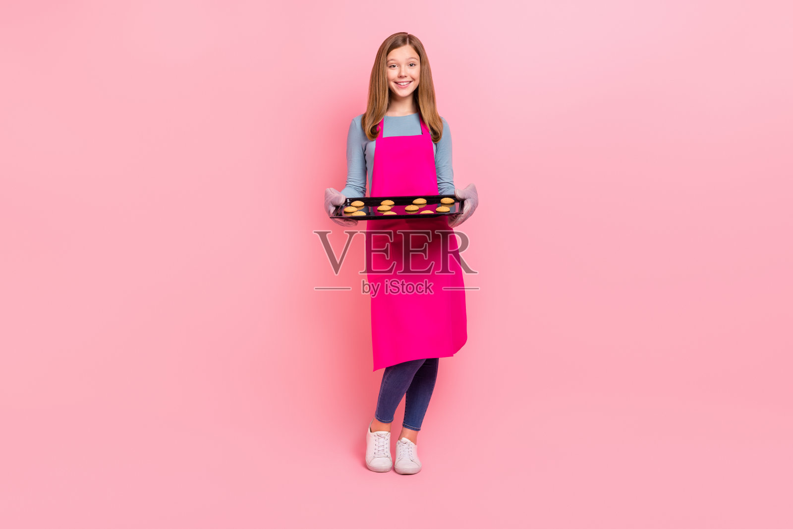 全身身材的迷人时尚女孩，手持托盘，盛放自制饼干，背景为粉色柔和色调。照片摄影图片