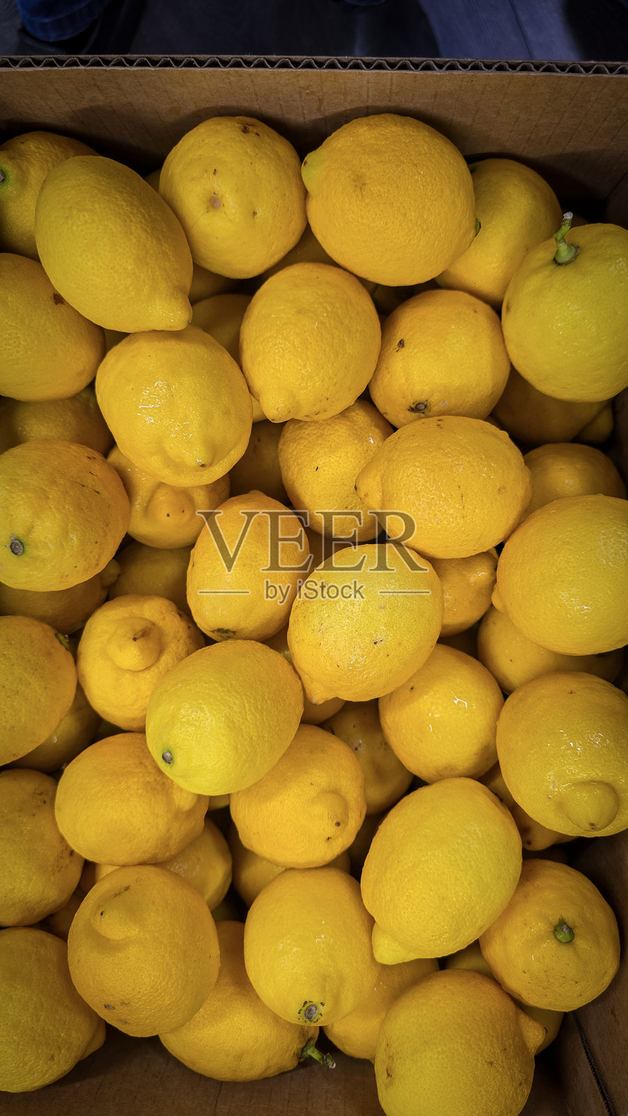 新鲜的黄色柠檬堆放在一个盒子里，展现出鲜艳的色彩和质感。柠檬堆。新鲜成熟的柠檬俯视图，富含维生素C，自然新鲜的柠檬堆。照片摄影图片