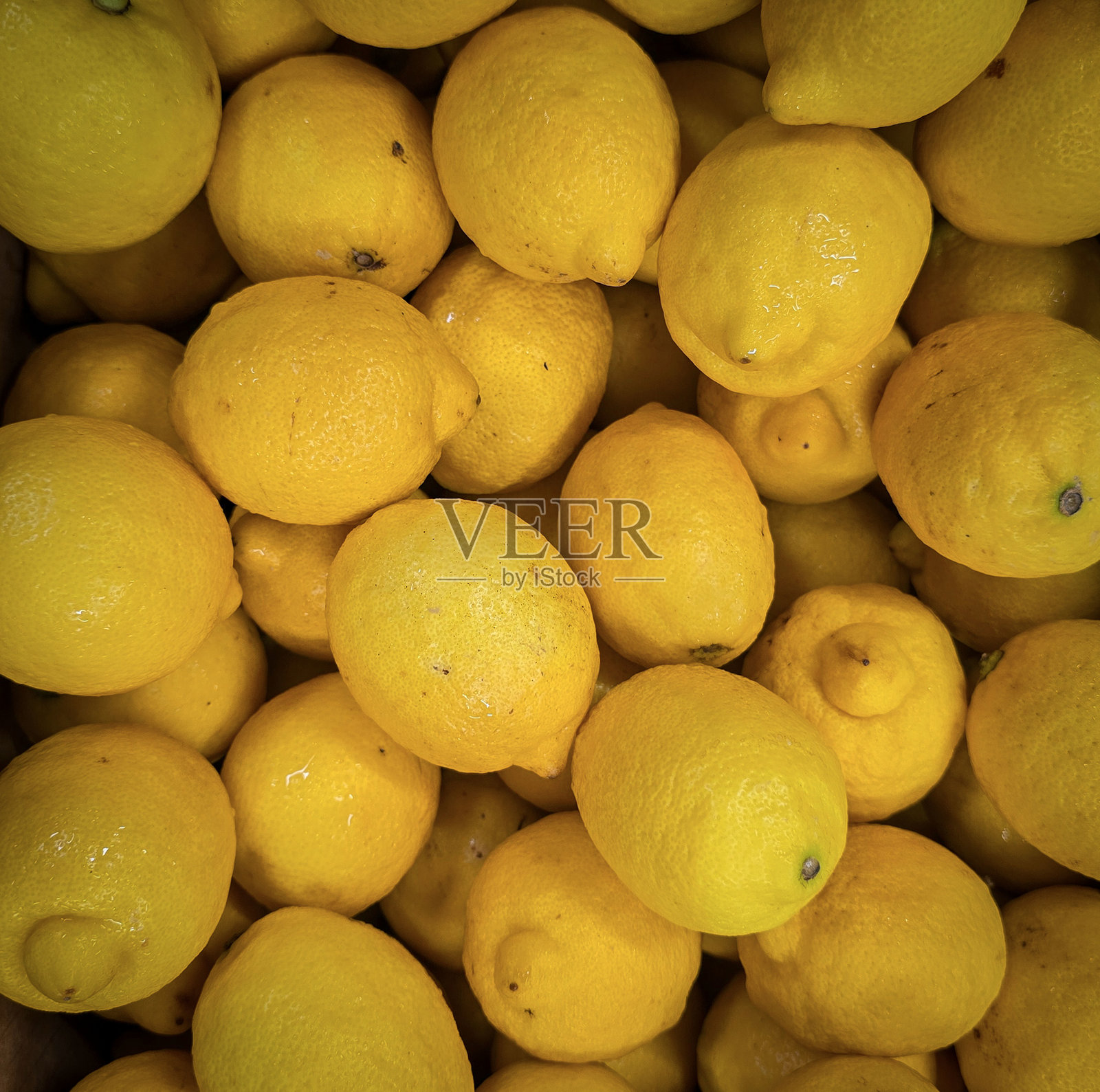 新鲜的黄色柠檬堆放在盒子里，展现出鲜艳的色彩和质感。柠檬堆。新鲜成熟的柠檬俯视图，色彩丰富，富含维生素C，自然新鲜的柠檬堆。照片摄影图片
