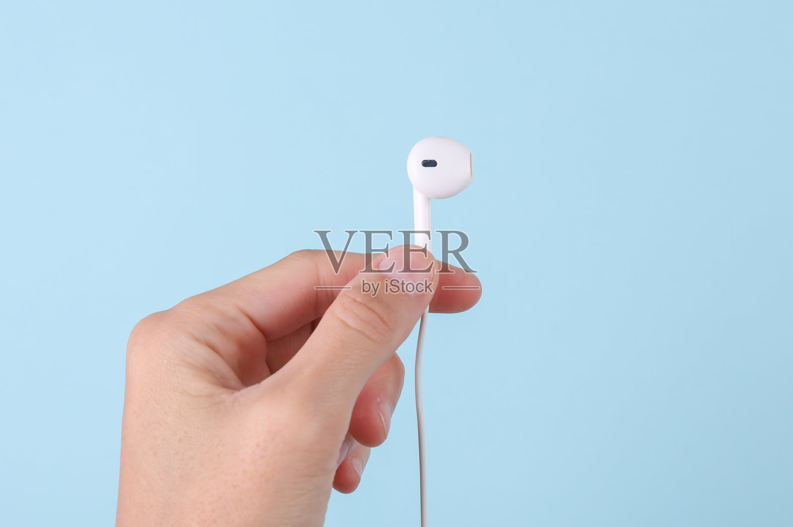 女性手握着蓝色背景上的有线耳机照片摄影图片
