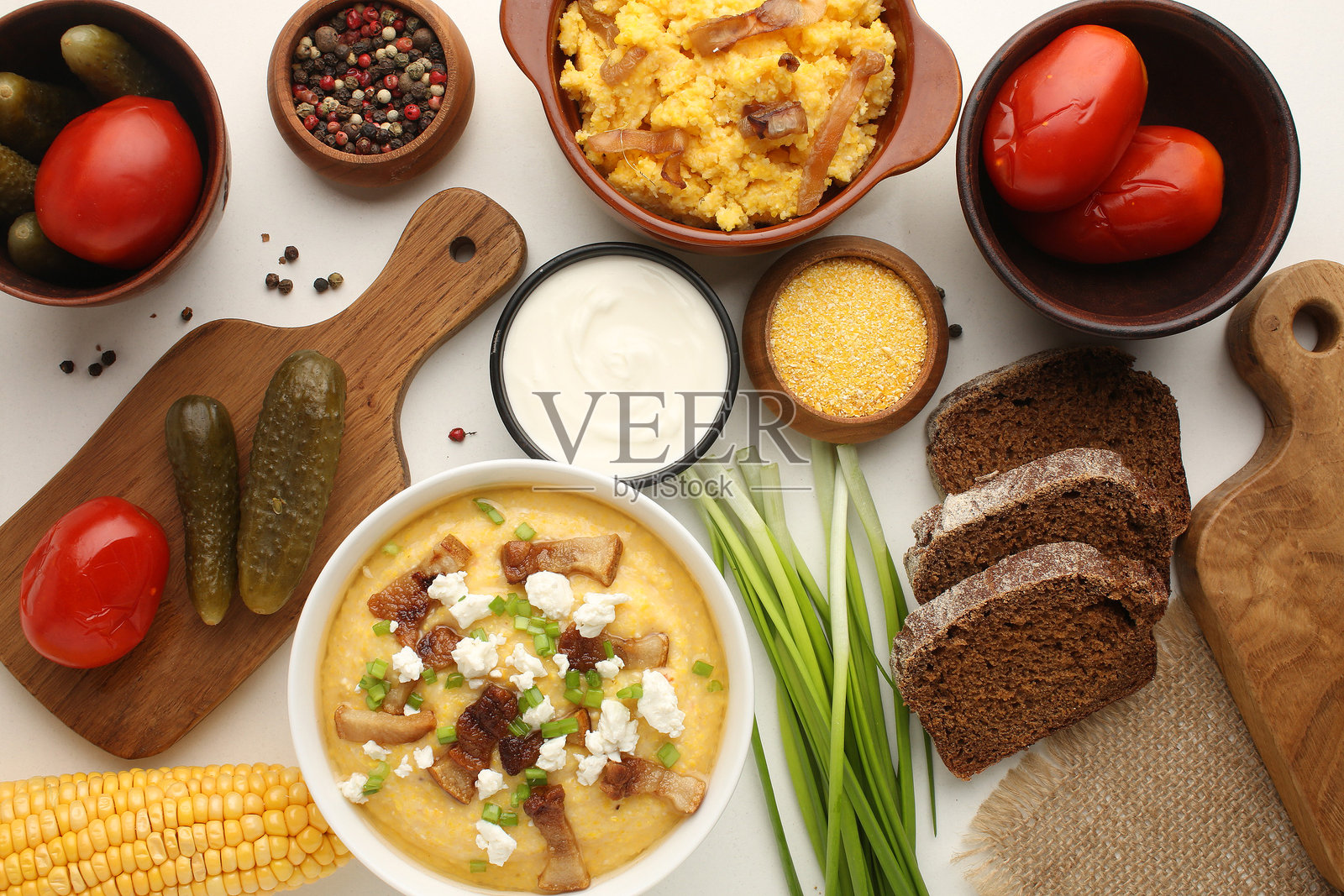 传统乌克兰食品玉米粗粒粥放在陶土锅中。陶碗里的玉米粉和成熟的玉米棒。浅色背景。特写镜头。从上方视角。照片摄影图片