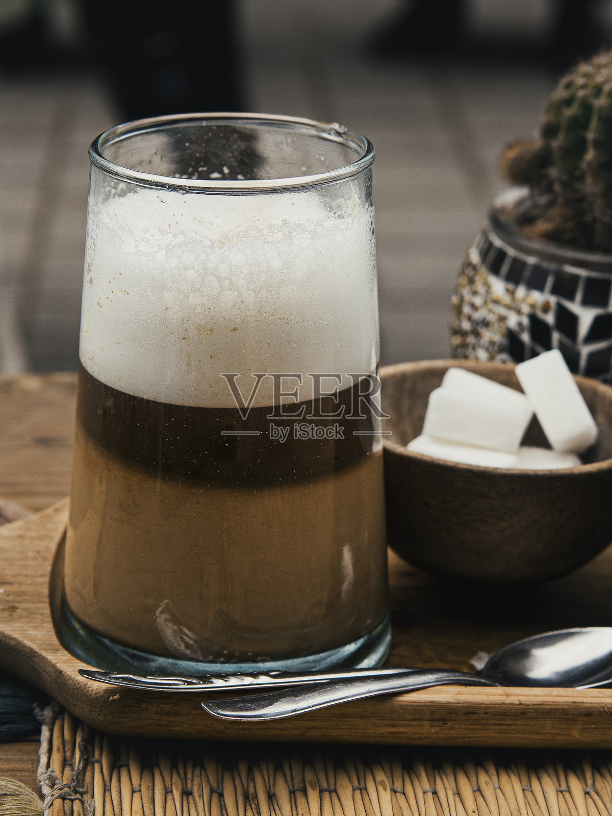 摩洛哥传统分层“Nous Nous”咖啡，杯中有奶油泡沫，配有方糖，放在一个质朴的木托盘上 – 在摩洛哥埃萨乌伊拉的舒适户外咖啡馆场景照片摄影图片