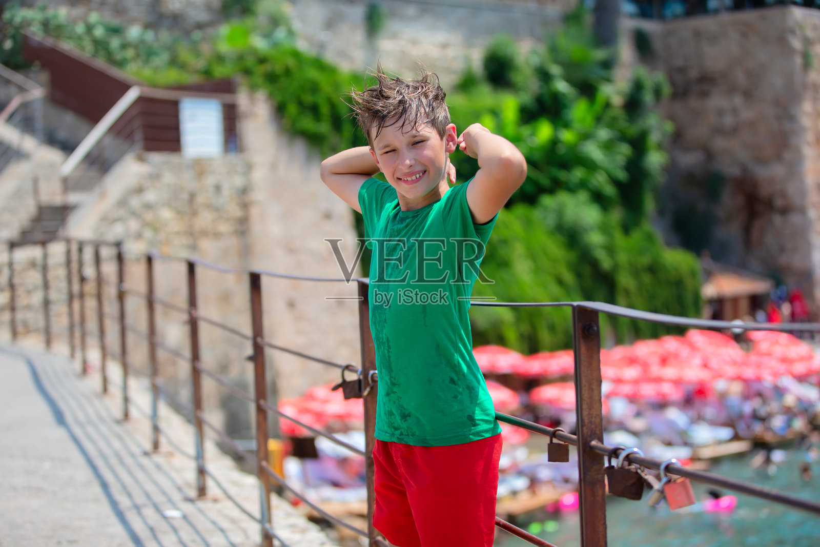 穿着绿色T恤的少年游客在模糊的海滩背景前。照片摄影图片