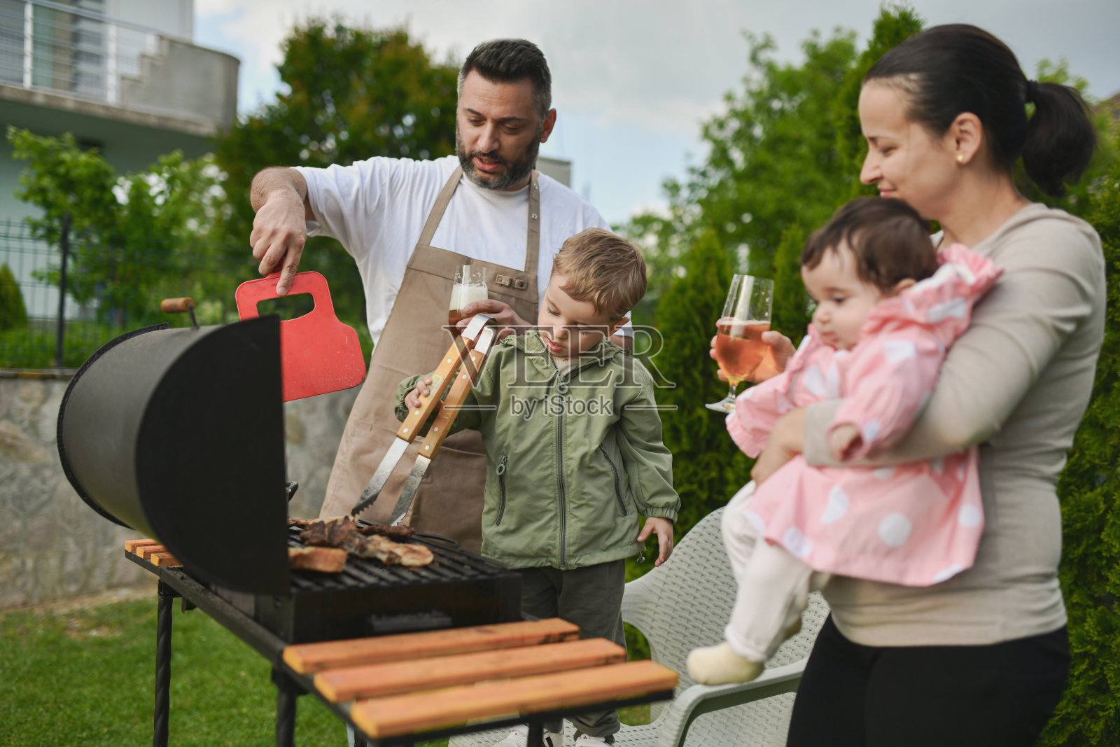 父母看着正在尝试帮助烧烤准备的幼儿男孩照片摄影图片