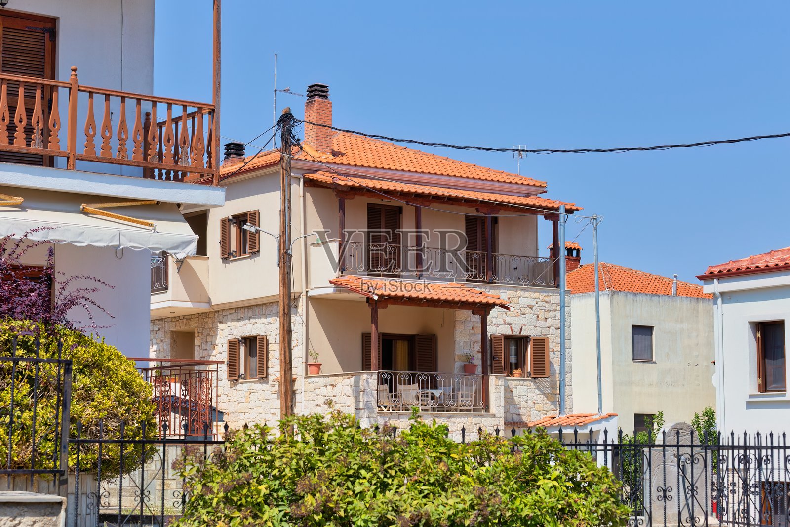 一栋阳光明媚的两层建筑，红色瓦屋顶，坐落在绿意盎然的环境中。照片摄影图片