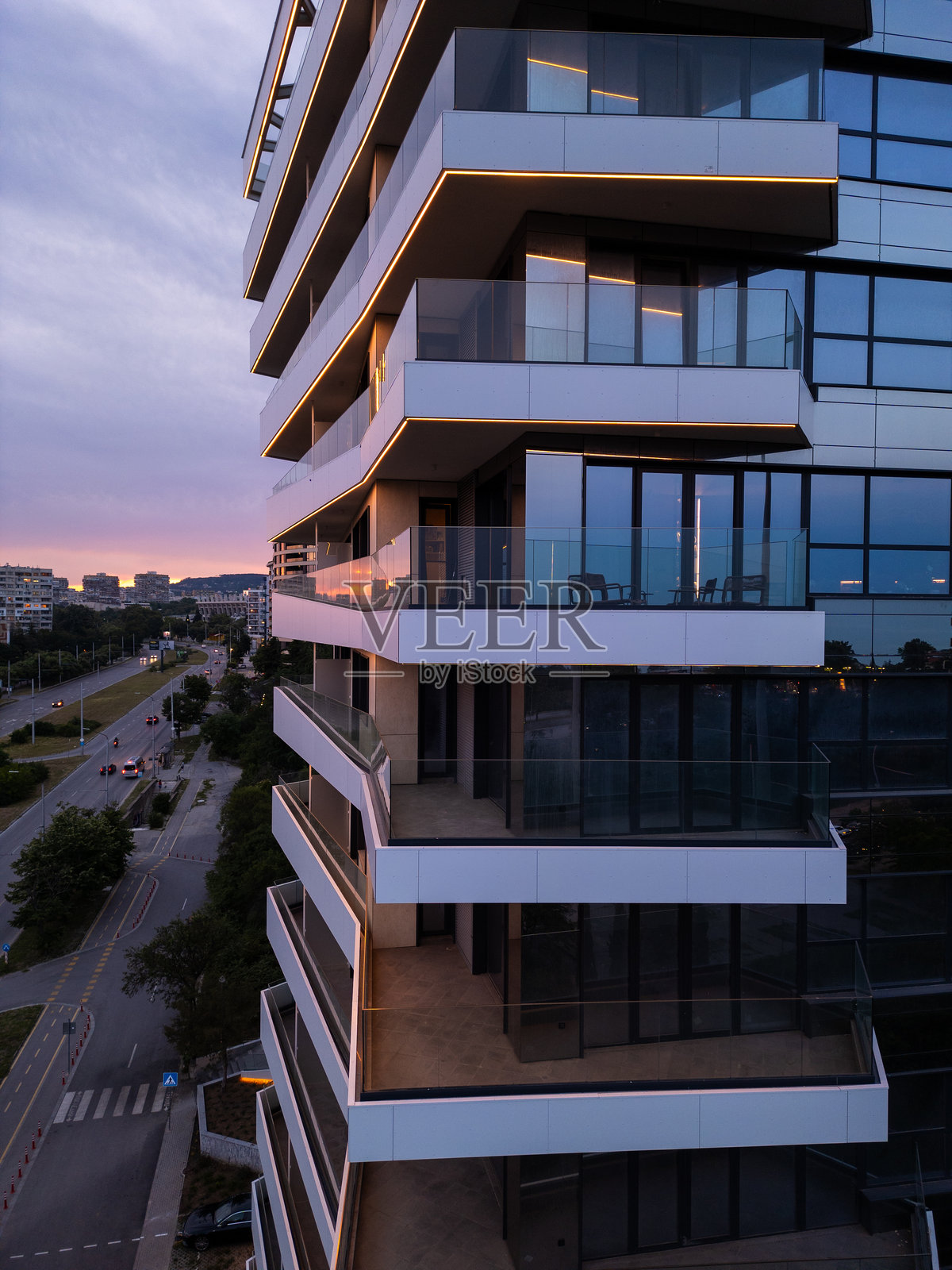 现代住宅建筑，配有玻璃阳台和LED灯光，夕阳下的景象。城市建筑与城市生活概念，柔和的天空倒影和傍晚氛围。照片摄影图片