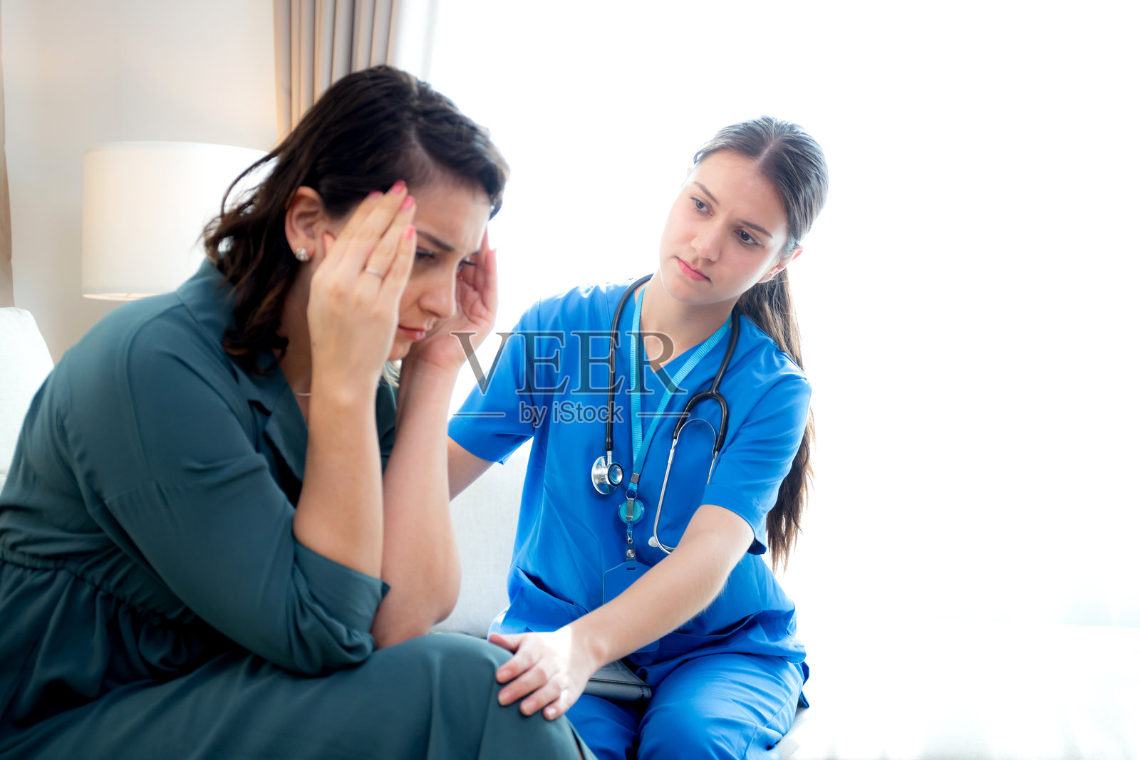 年轻的白人女性护士安慰一位感到压力和担忧的患者，医生在一旁鼓励和安慰这位癌症患者，流露出担忧和悲伤，涉及医疗和保险问题。照片摄影图片