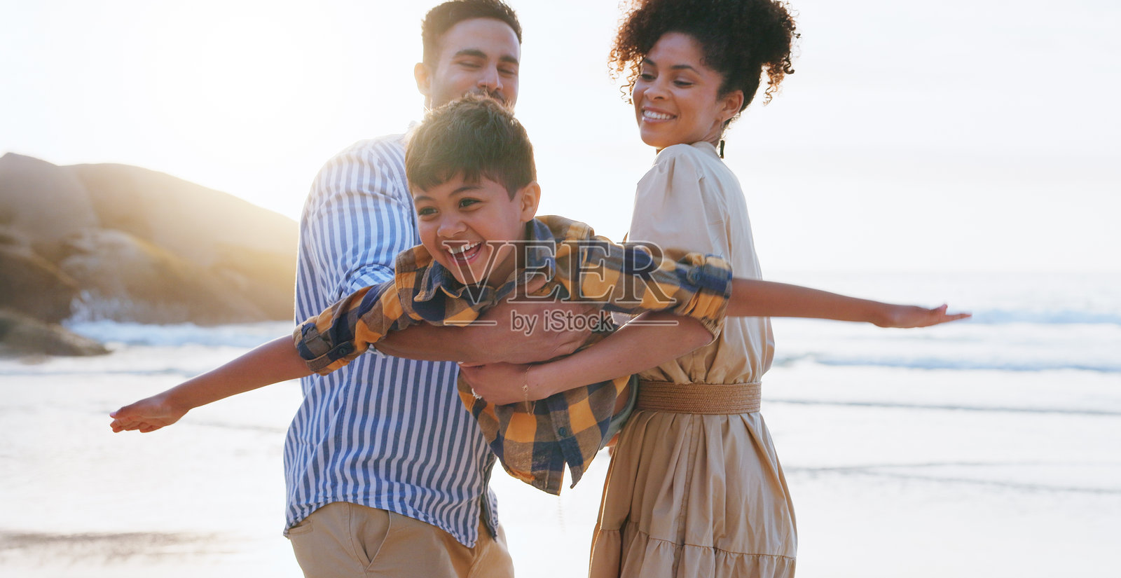 父母、男孩和在海滩上升起的飞机，快乐而顽皮地玩游戏，享受假期中的爱与亲密。人们，男人和女人与孩子，兴奋地度假，夏天和海洋。照片摄影图片