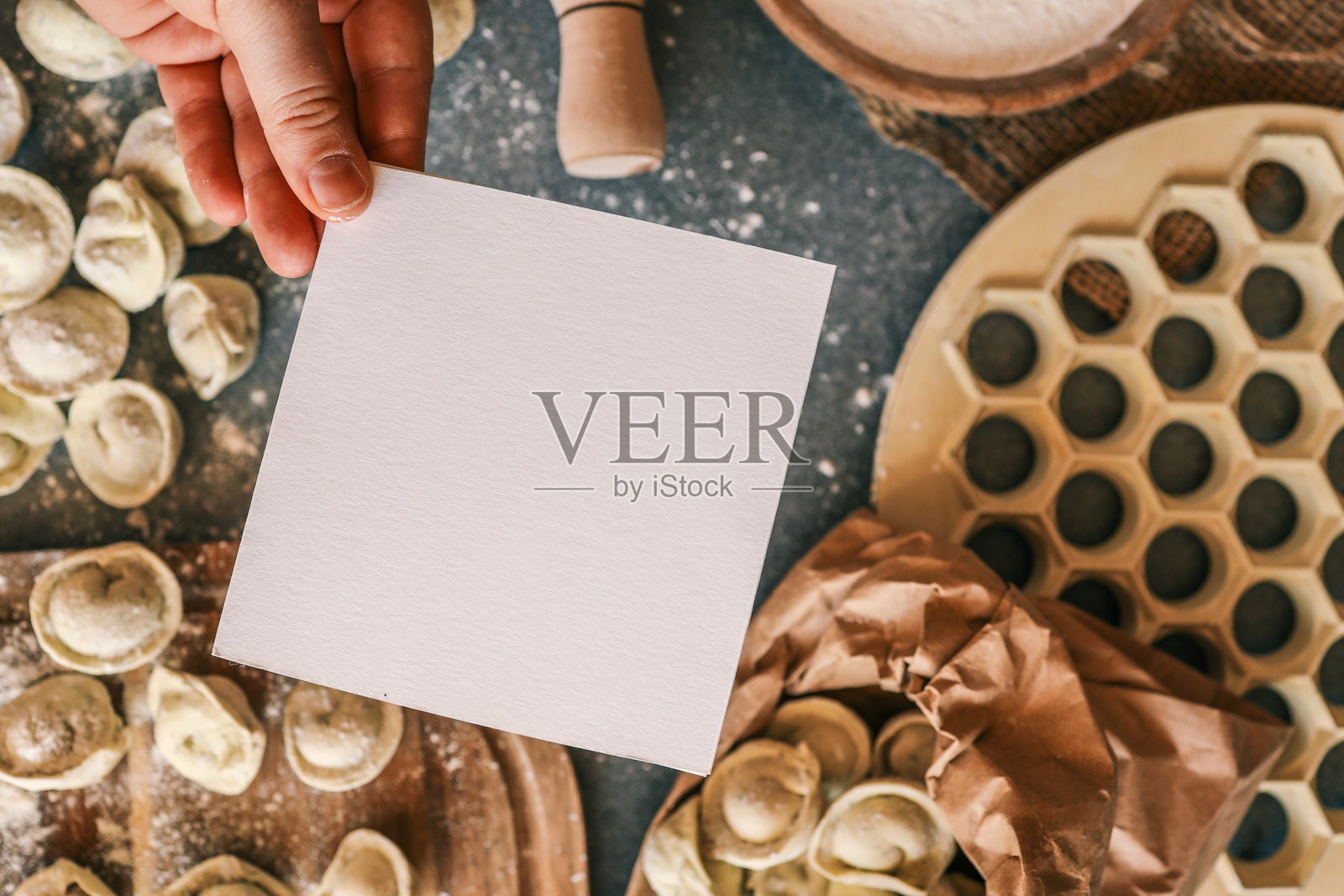 一张空白的白色卡片悬在乡村风格的厨房桌子上，桌上有自制的饺子、面粉和烹饪用具，非常适合写食谱笔记或邀请函。照片摄影图片