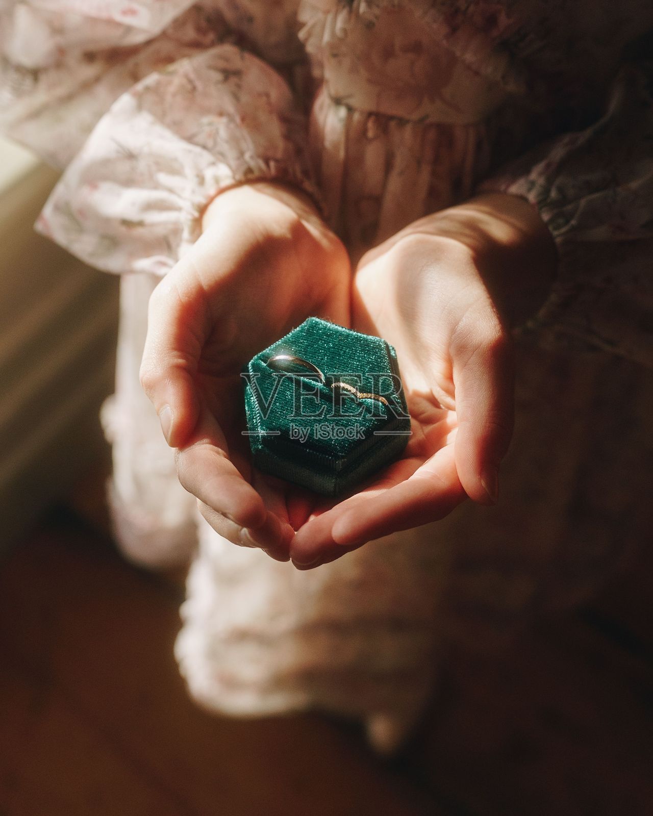 女人在柔和的光线下手持一个绿色天鹅绒戒指盒。照片摄影图片