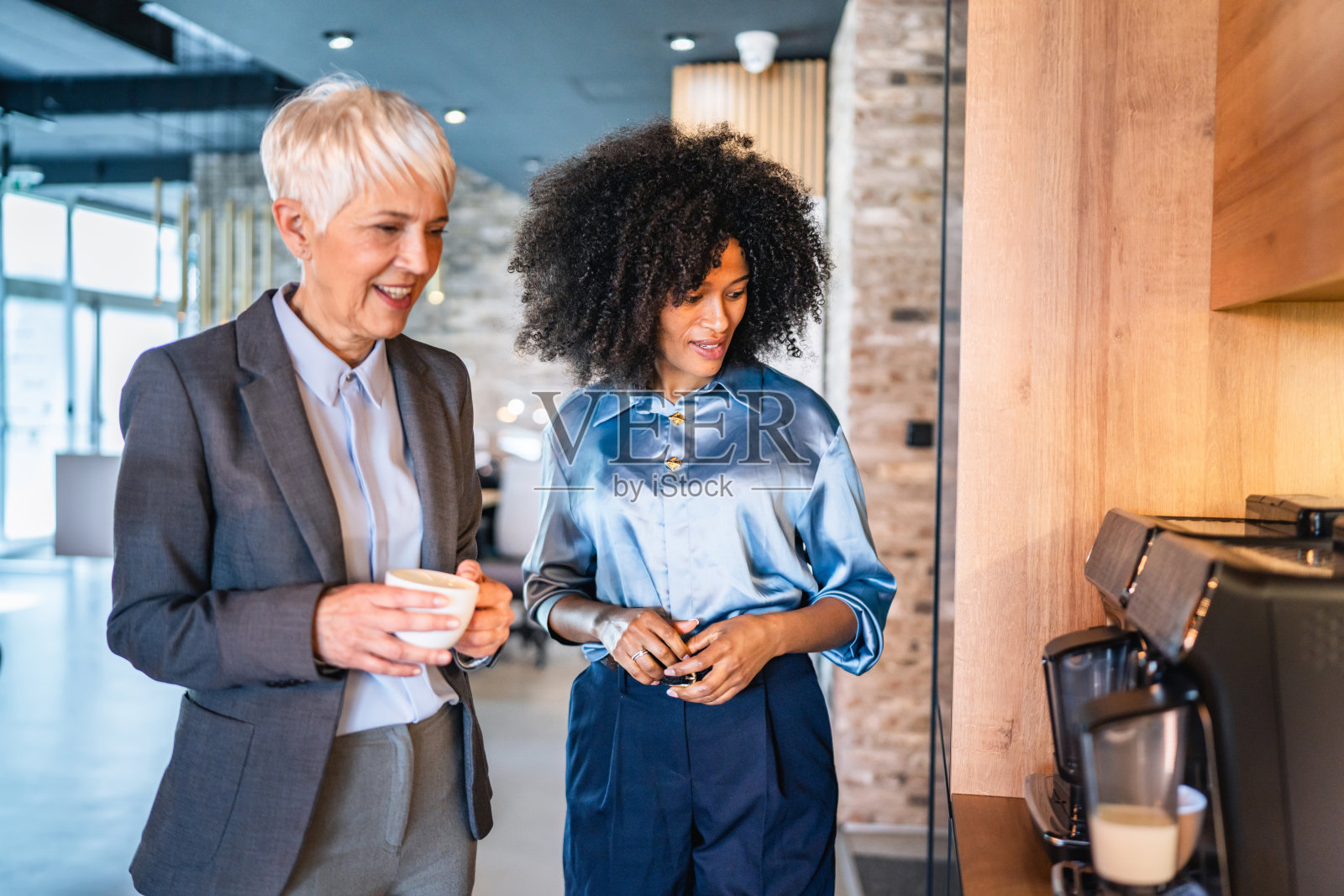女同事们在现代咖啡机旁聊天，等待咖啡。照片摄影图片