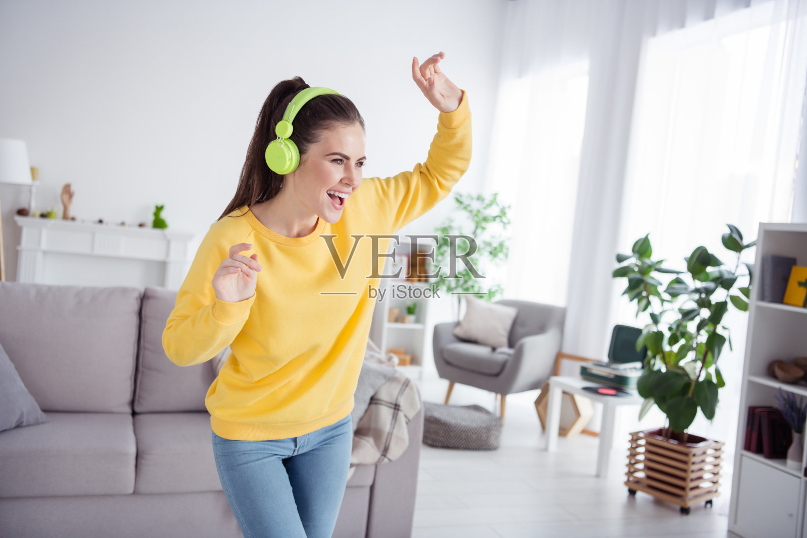 穿着舒适黄色毛衣的快乐积极无忧的女士在室内享受派对舞蹈。照片摄影图片