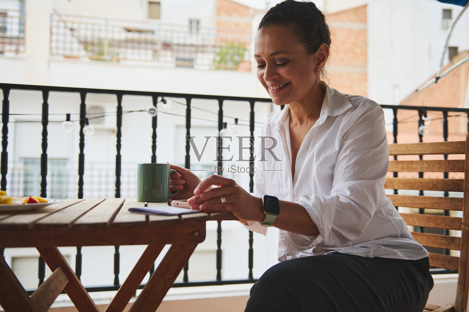女人在阳台上享受早晨咖啡，同时使用智能手机放松和提高工作效率照片摄影图片