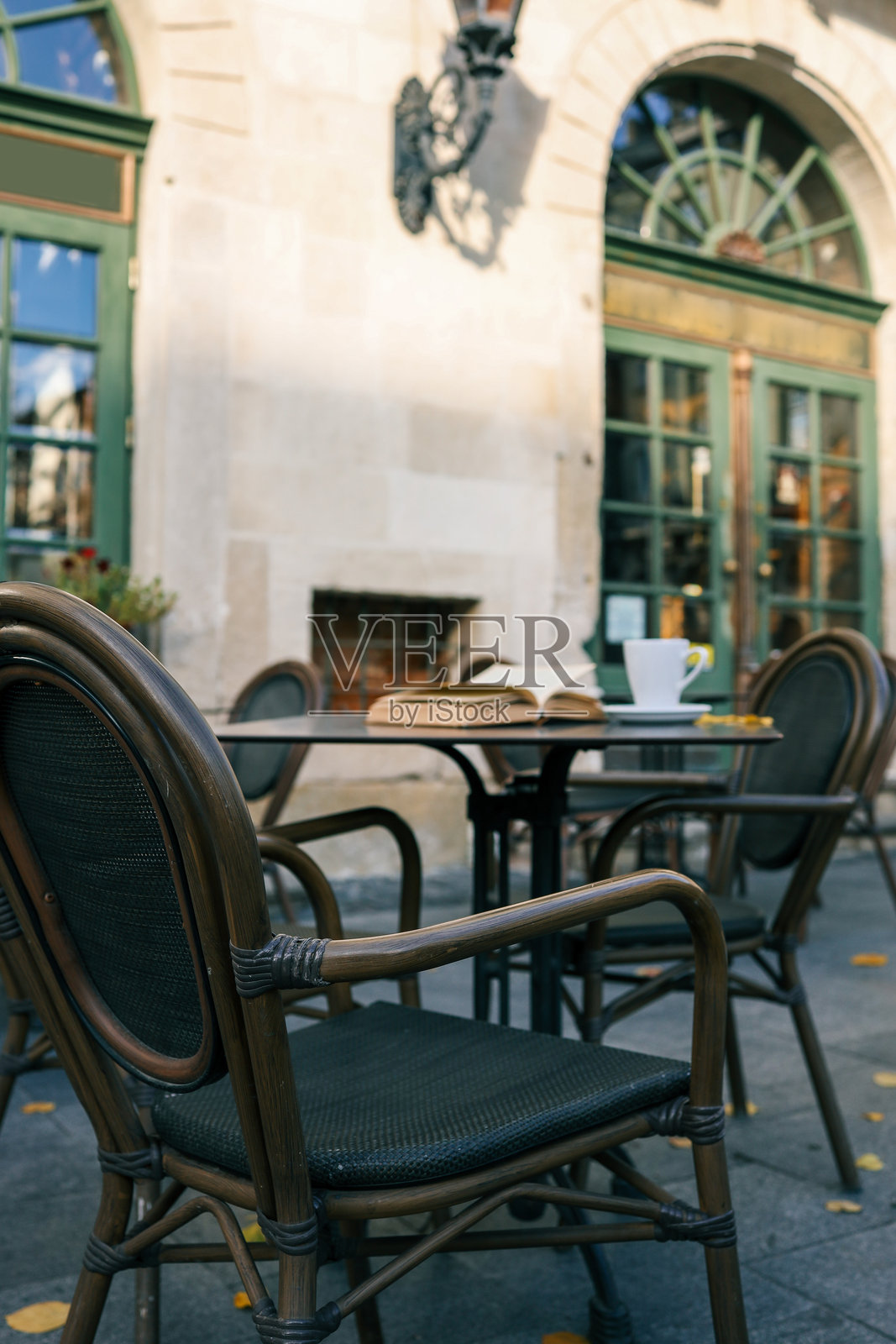 户外咖啡桌上放着一本打开的书和一杯咖啡。空椅子、温暖的阳光和迷人的复古建筑营造出宁静的氛围。照片摄影图片