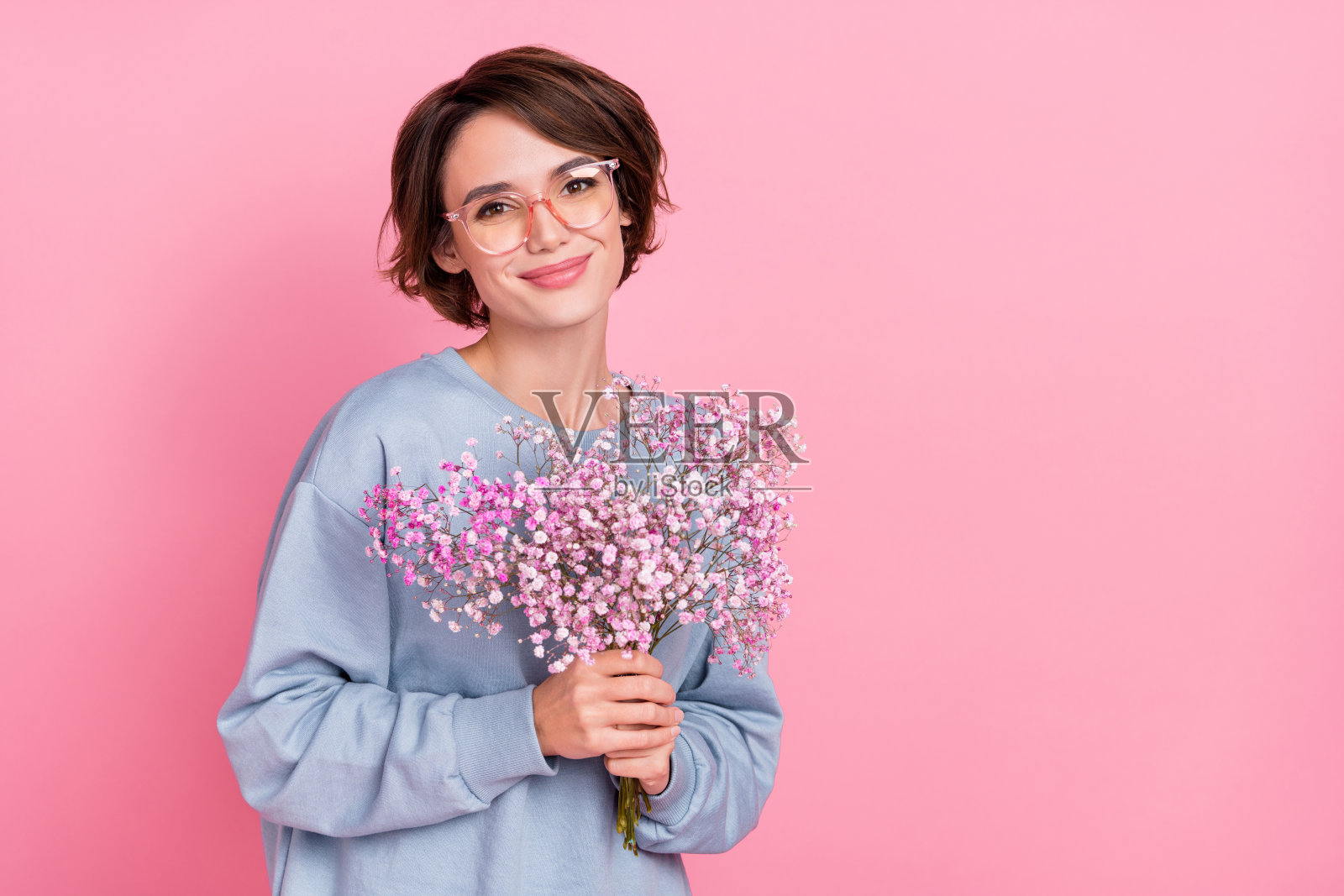 可爱的女孩微笑着手捧鲜花，背景为粉色柔和色调，留有空白空间。照片摄影图片