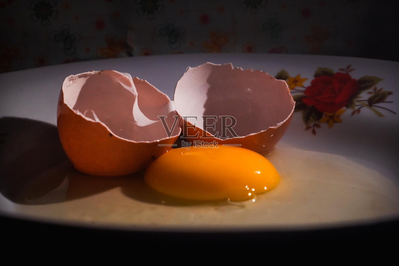 低光下的花卉盘子上的破蛋壳和生蛋黄照片摄影图片