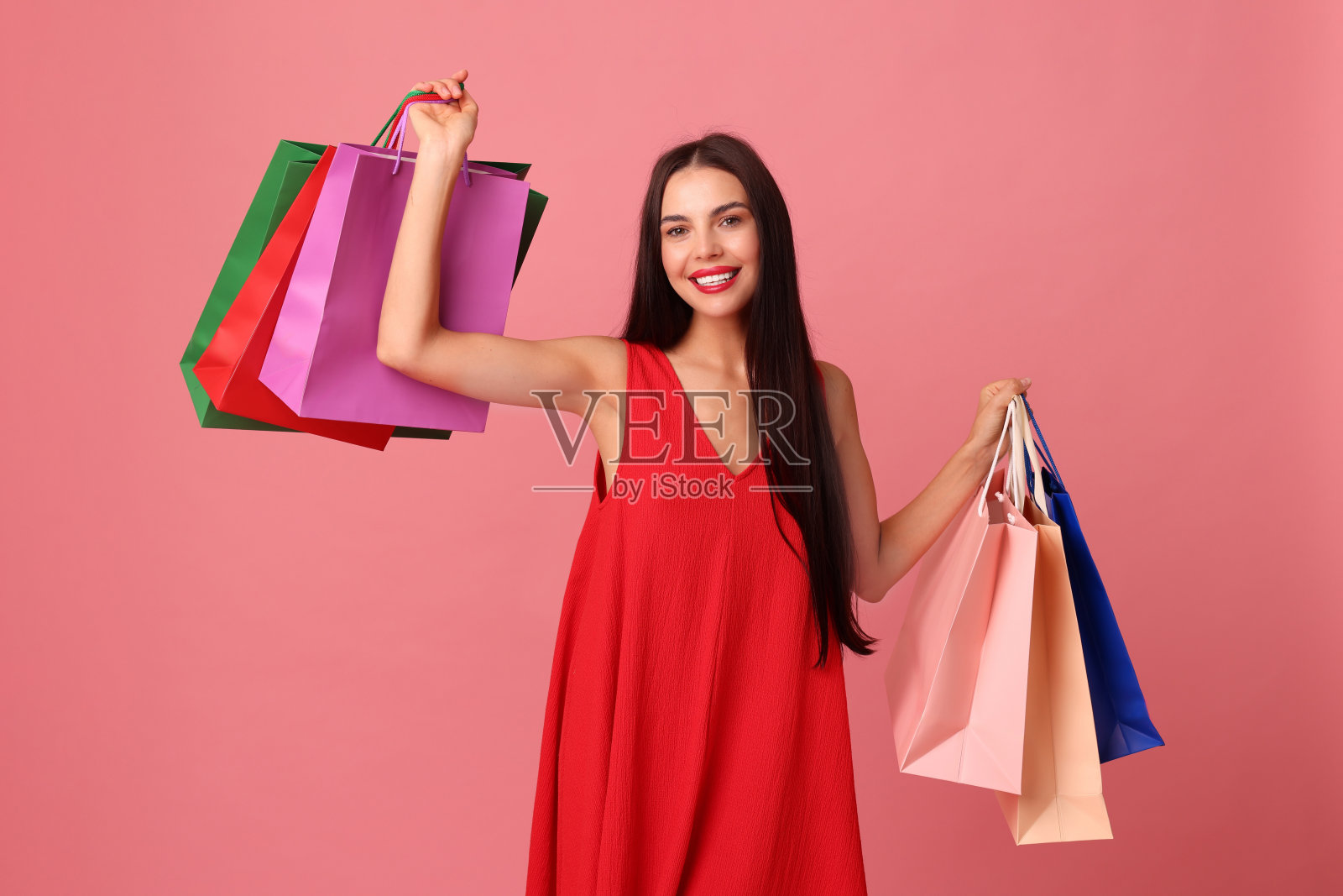 微笑的女性手持五彩购物袋，背景为粉色照片摄影图片