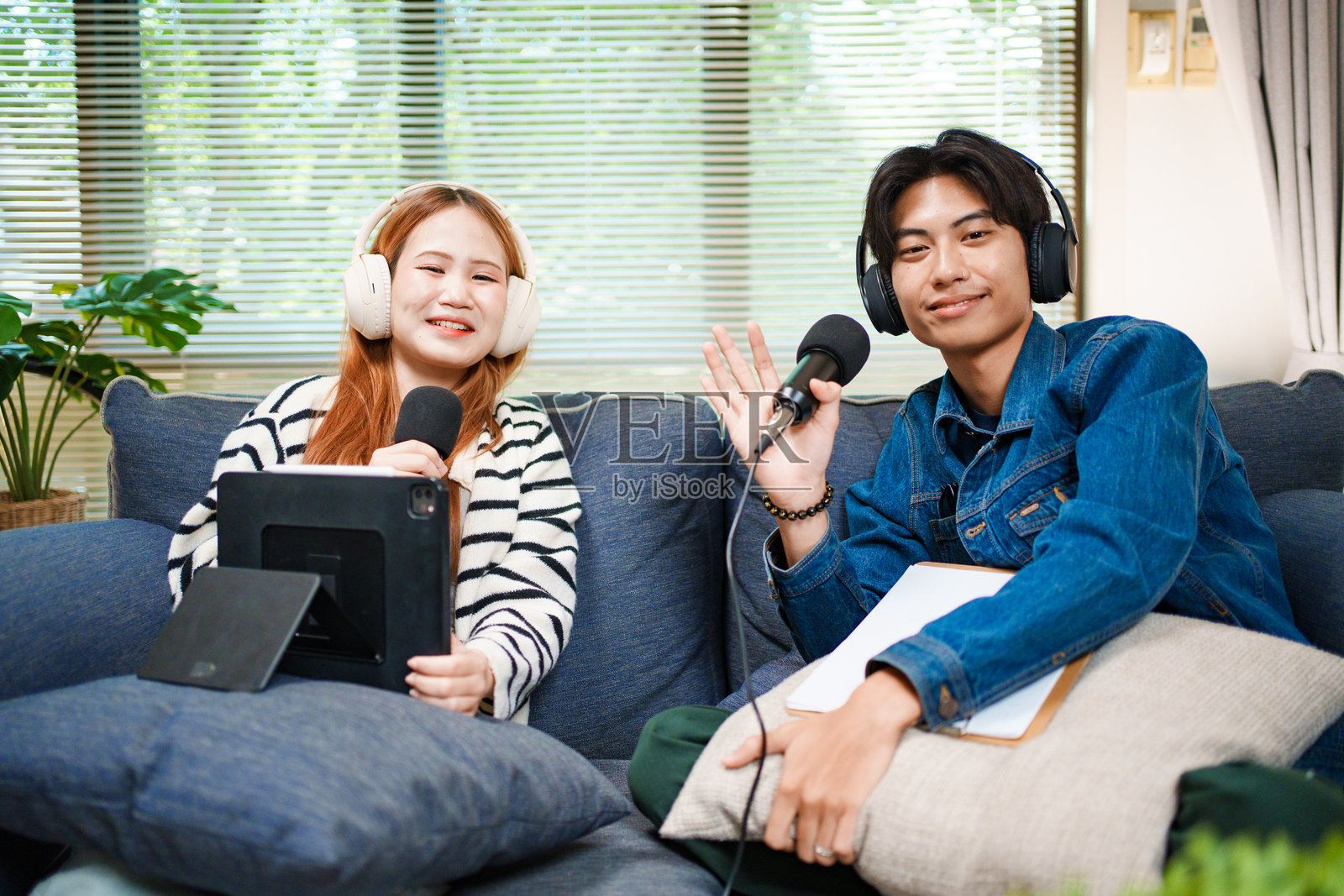 友好的播客主持人挥手向摄像机，佩戴着麦克风和耳机照片摄影图片