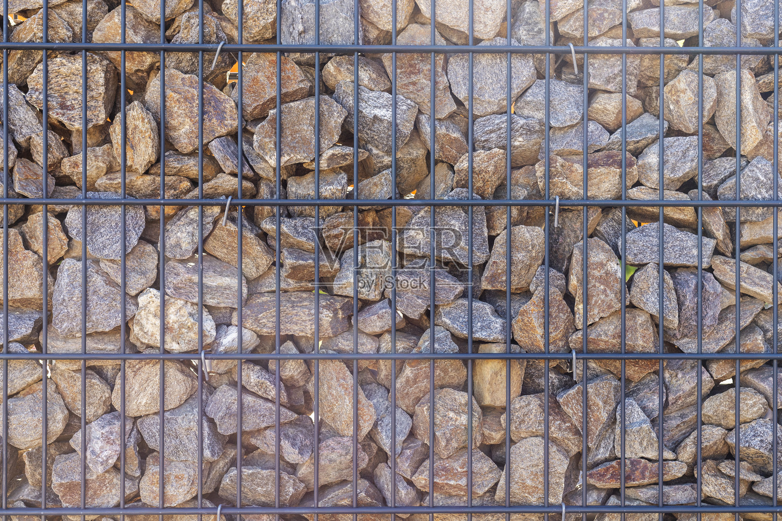 一面由不规则形状的岩石构成的墙壁，岩石被固定在黑色金属网格中。石头的大小和颜色各异，形成了一种自然的图案。照片摄影图片