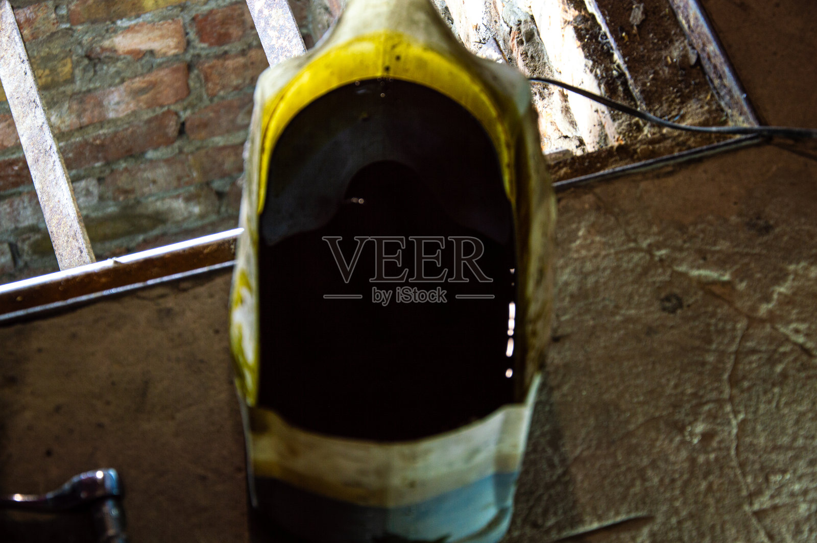 一个装满黑色机油的容器静静地放在混凝土表面上，旁边的窗户透进自然光照亮了它。照片摄影图片