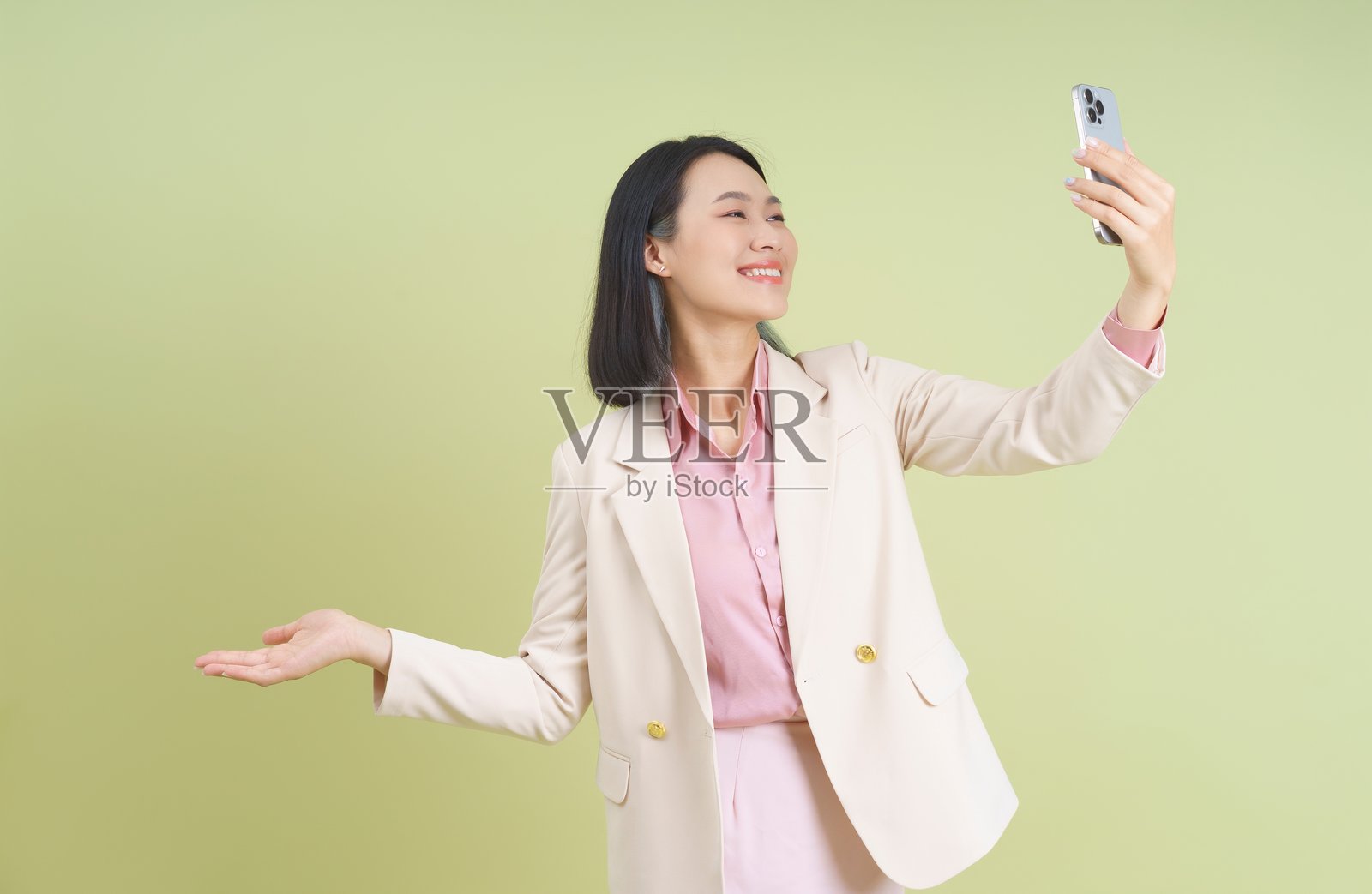 微笑的女性在现代工作室的绿色背景前自信地摆姿势拍自拍。照片摄影图片