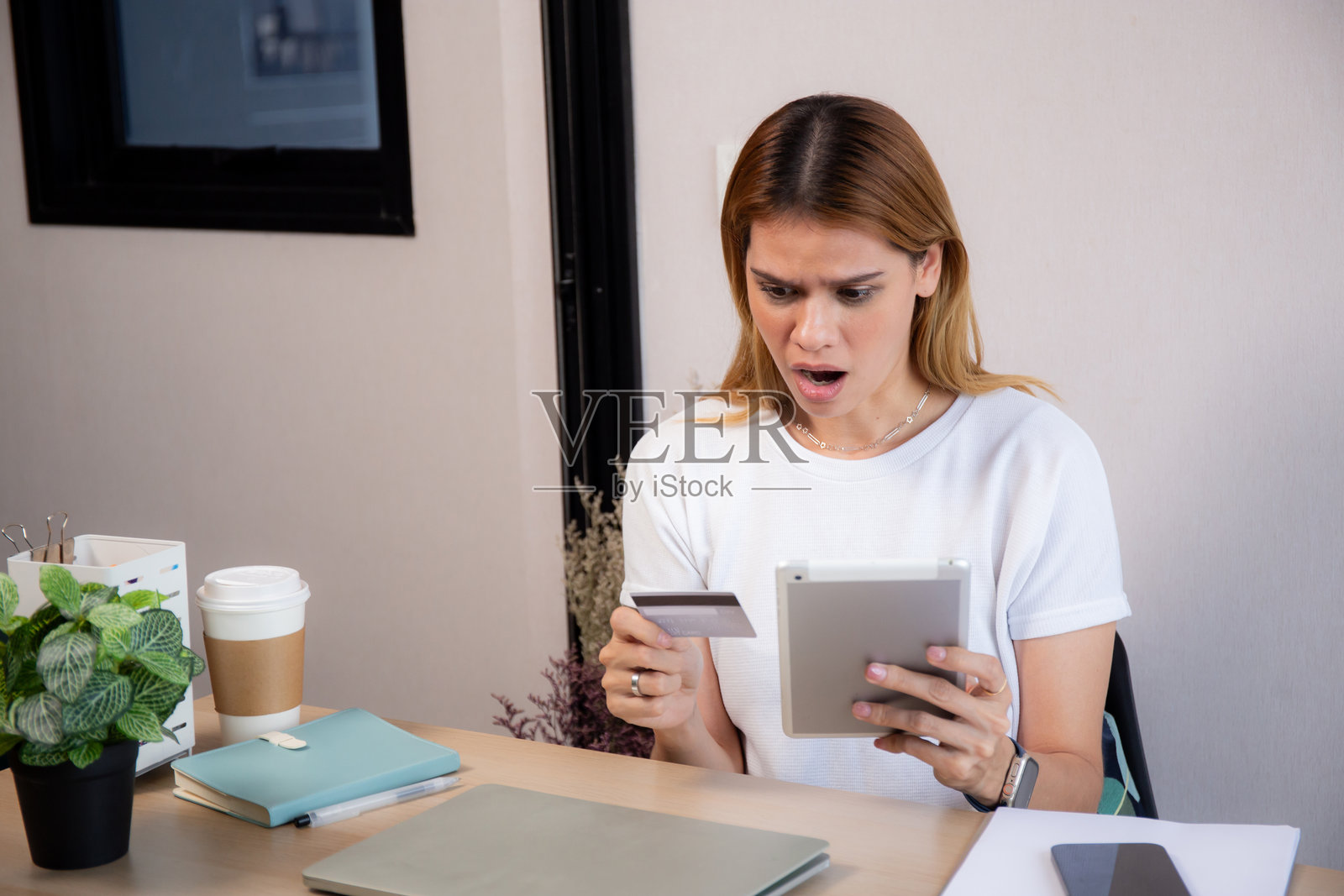 年轻的白人女性手持信用卡或借记卡，震惊和惊讶地看着平板电脑进行在线购物，女性在进行消费交易，商业与金融。照片摄影图片