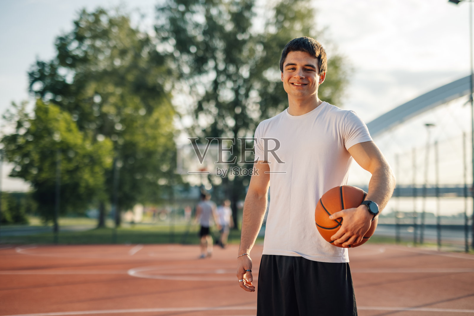 年轻的篮球运动员在户外球场微笑着握着篮球照片摄影图片